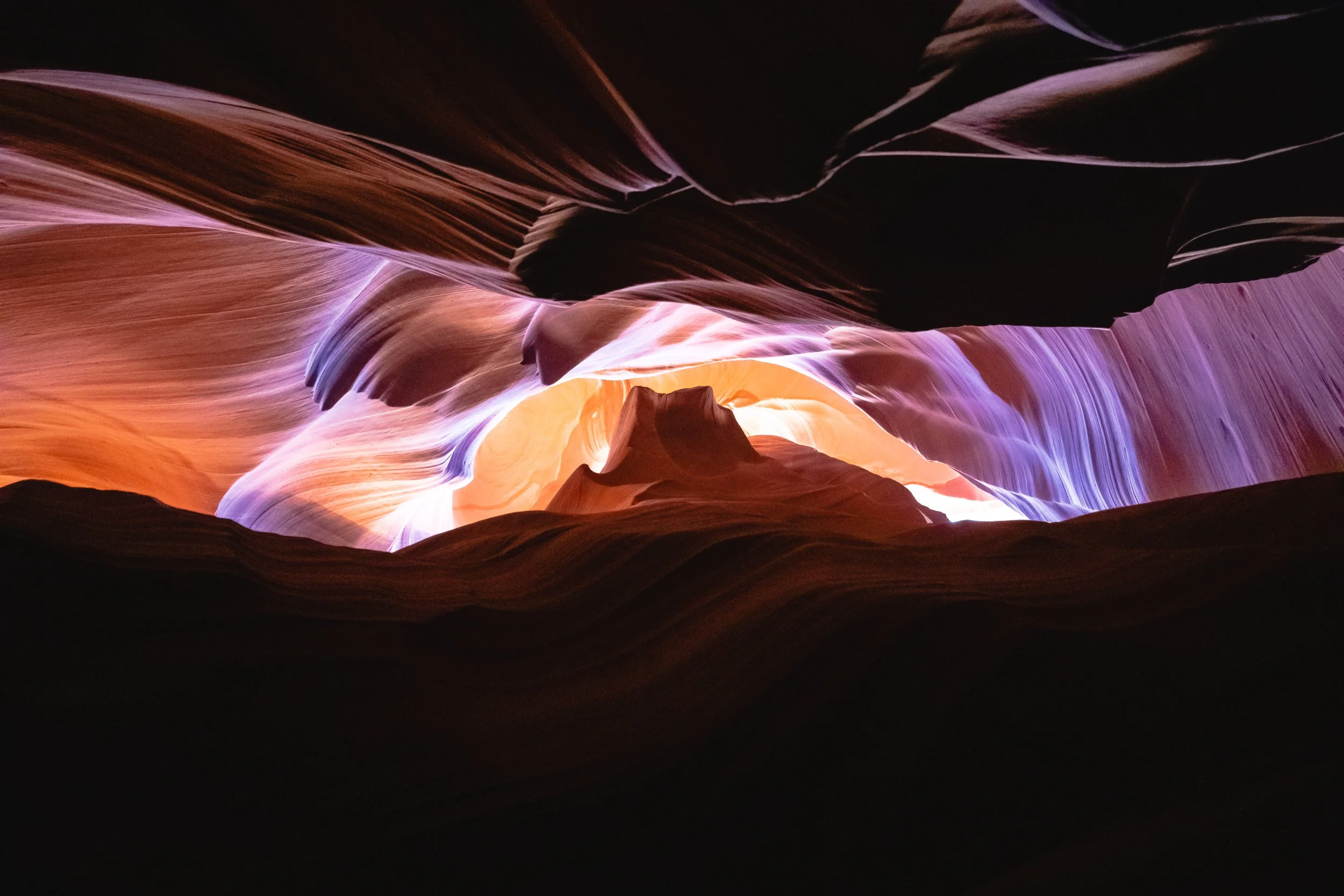 Colorful rock formations inside a canyon with smooth, flowing shapes and vibrant hues of orange, purple, and black.