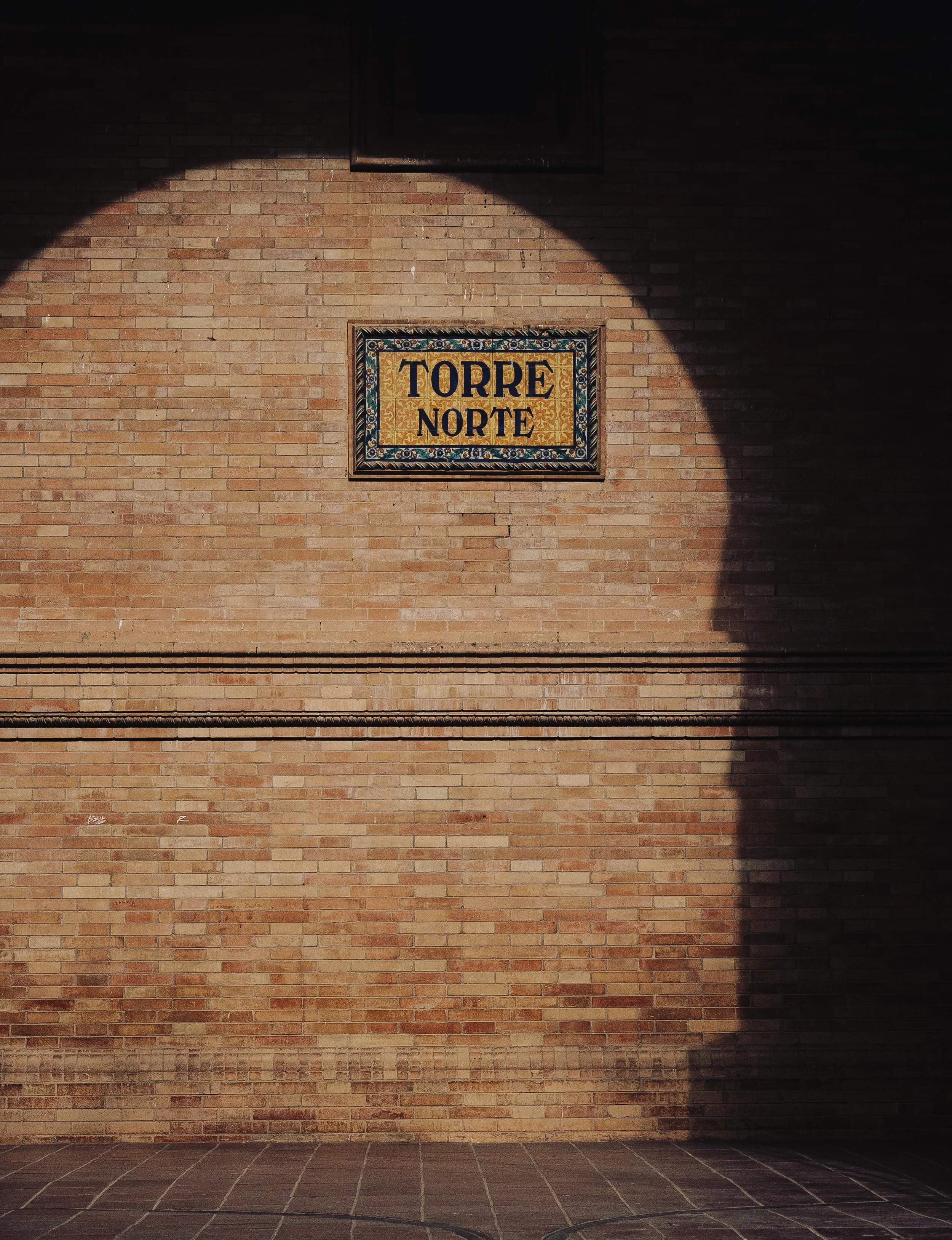 A brick wall with a decorative sign that reads 'TORRE NORTE' and part of a shadow cast across it.
