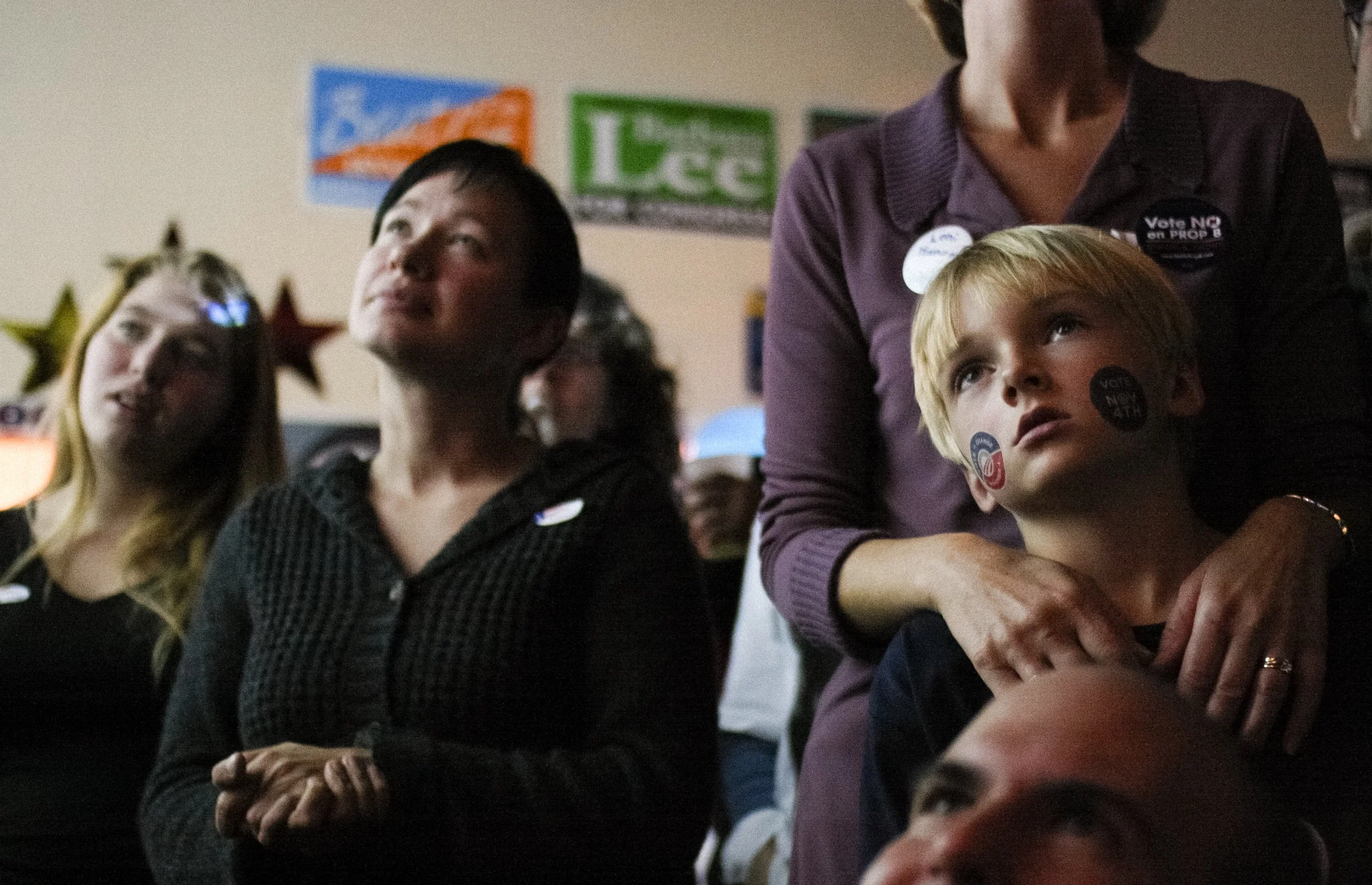 People gathered indoors at a political event, wearing campaign stickers and buttons supporting voting initiatives.