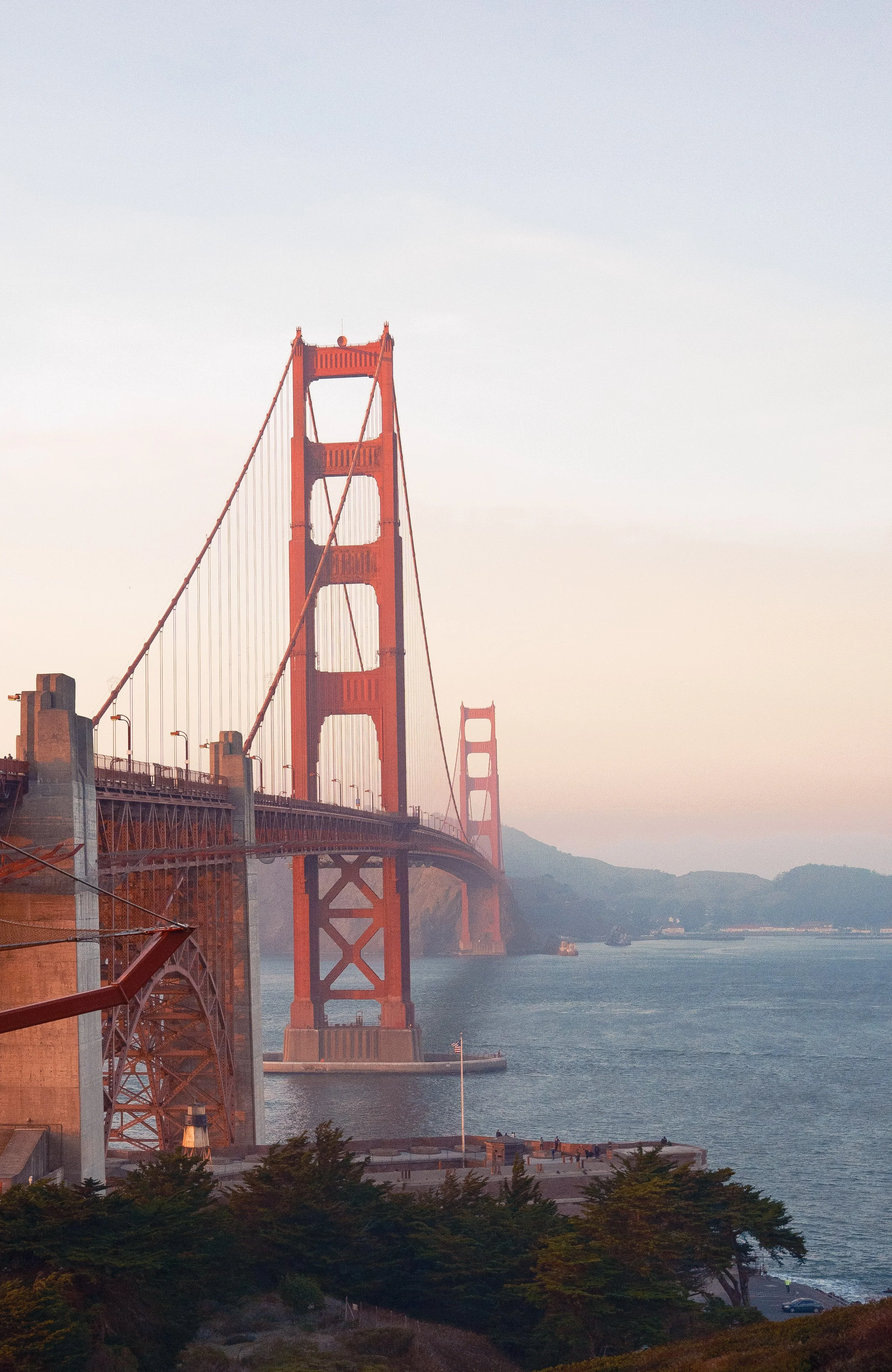 The Golden Gate Bridge in San Francisco during dusk with a hazy sky and mountains in the background.
