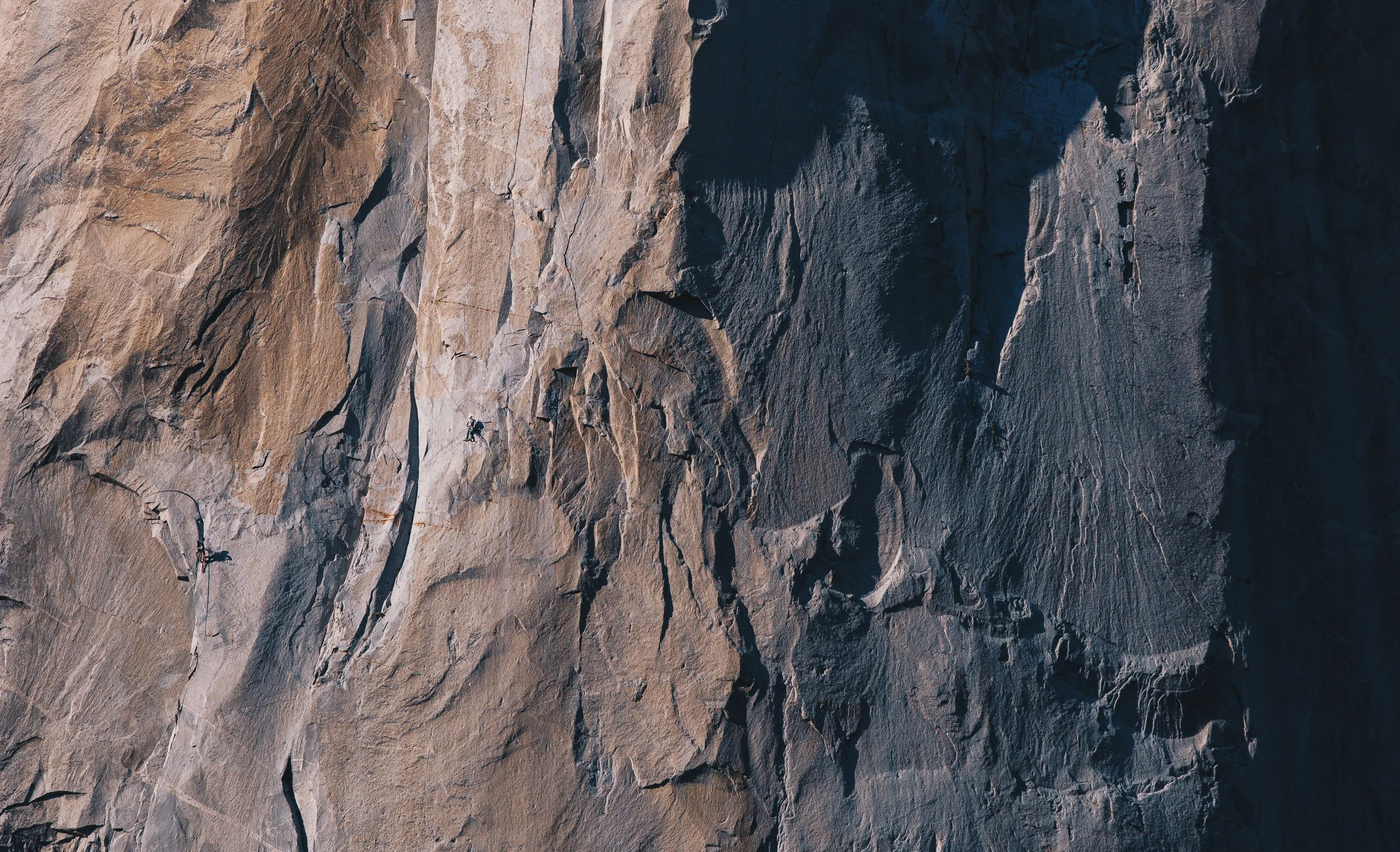 Close-up of a textured rock face with visible cracks and crevices, showing natural geological formations in shades of beige, brown, and gray.