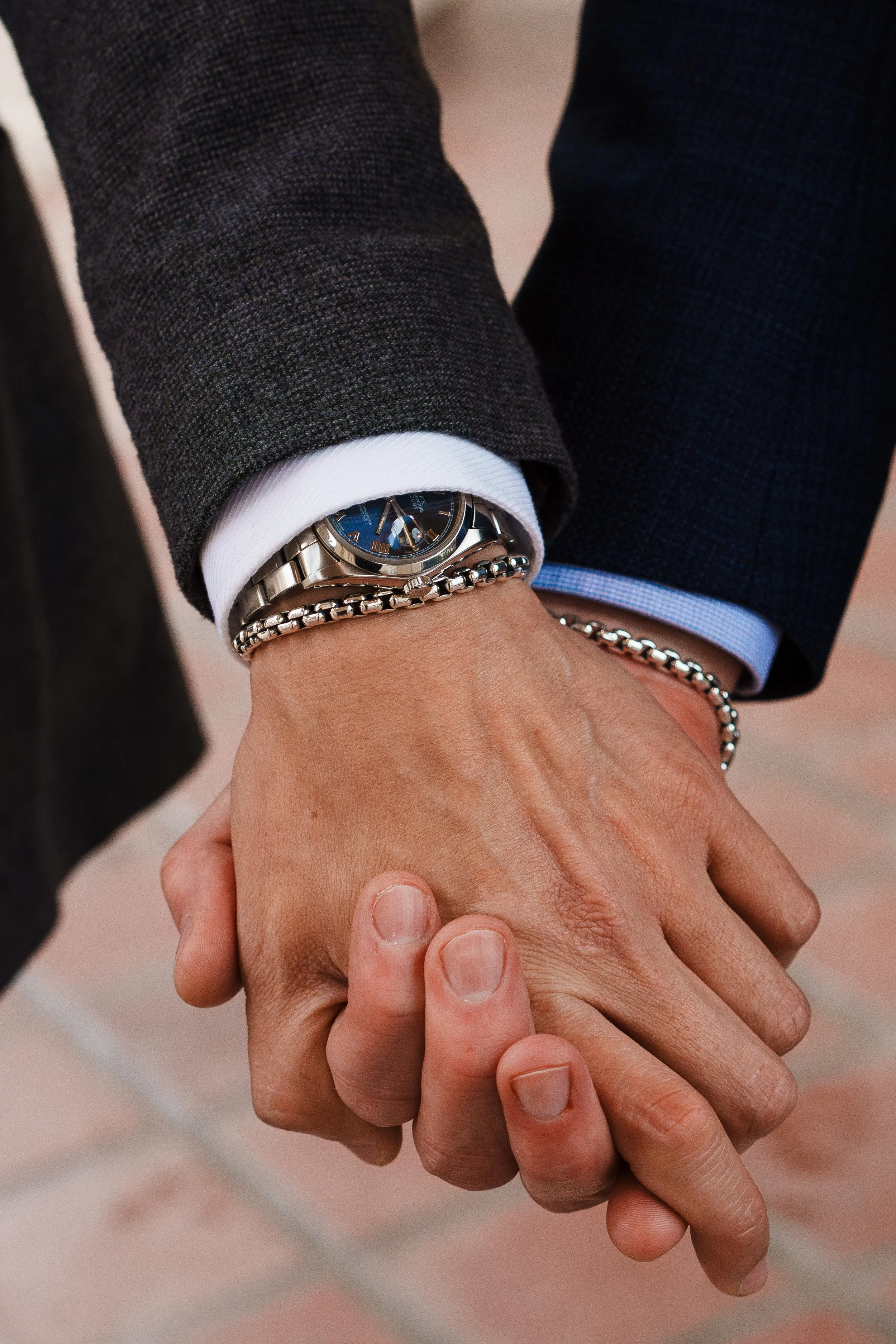 Two people holding hands, wearing formal business attire, with the focus on their hands and one person's wristwatch and bracelet.