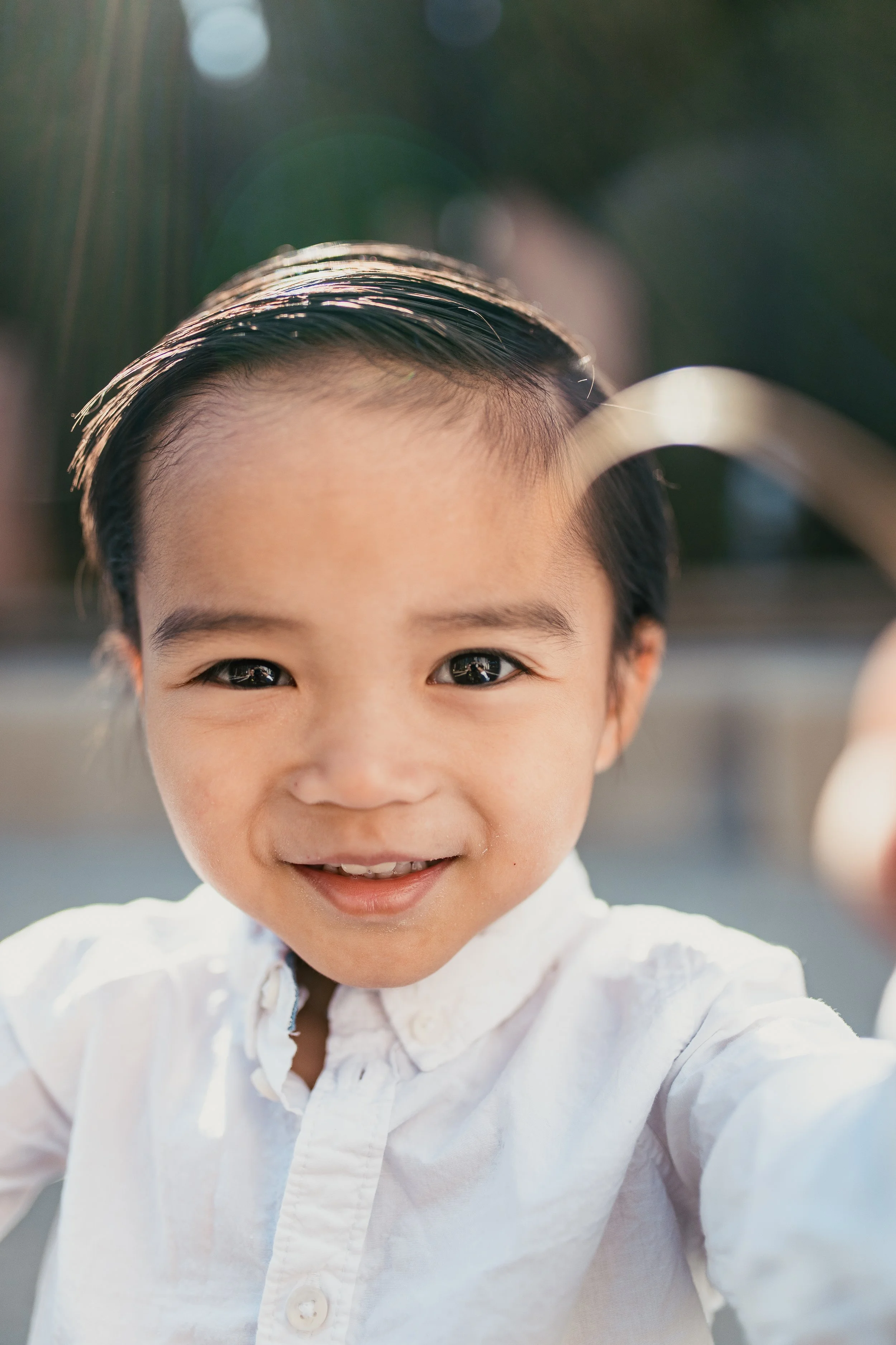 Close-up of a smiling young boy with neatly combed dark hair, wearing a white shirt with a ruffled collar.