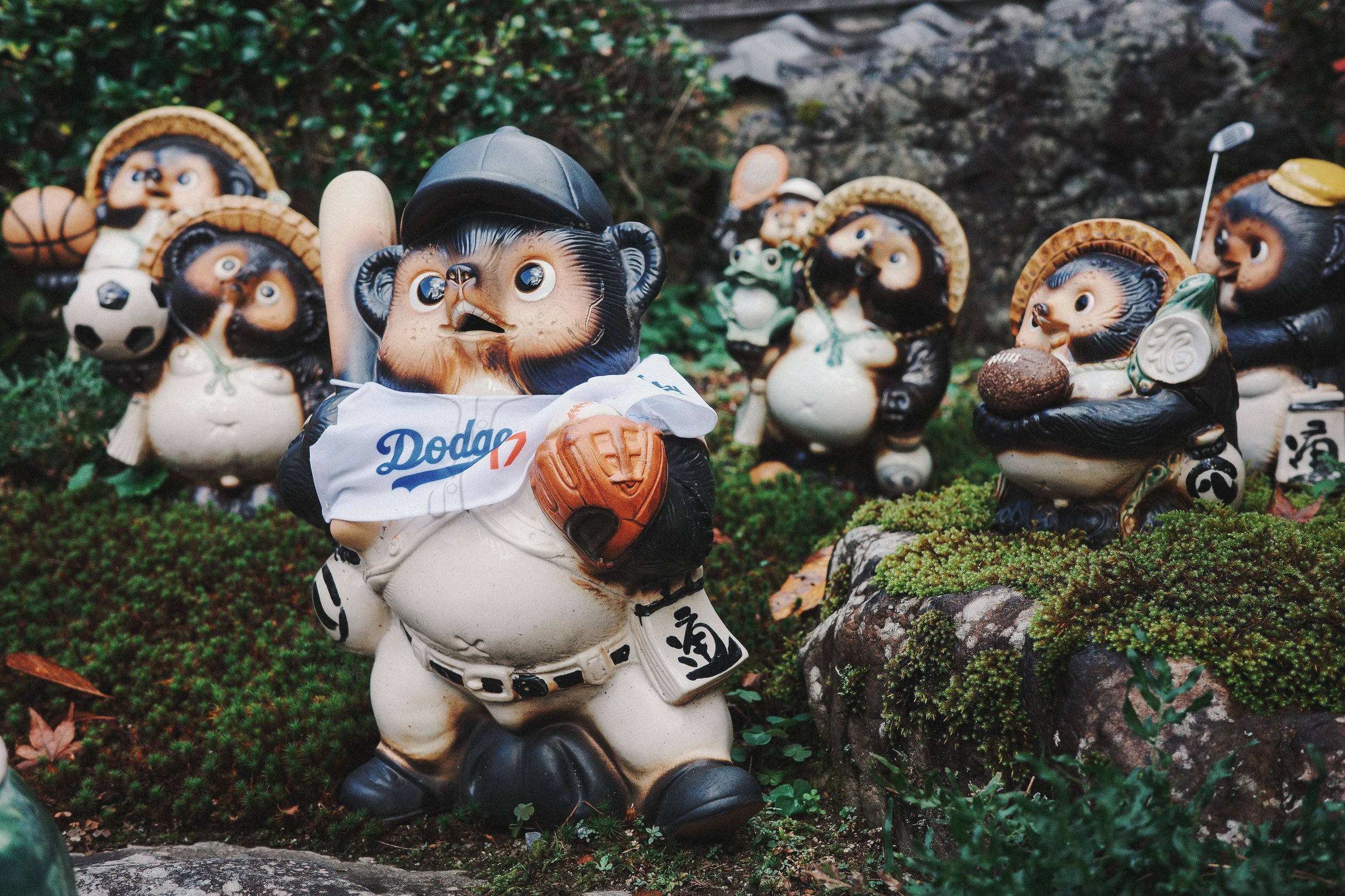 Garden ornaments of animated animal characters, including a tiger dressed as a baseball player, with a backdrop of green foliage and rocks.