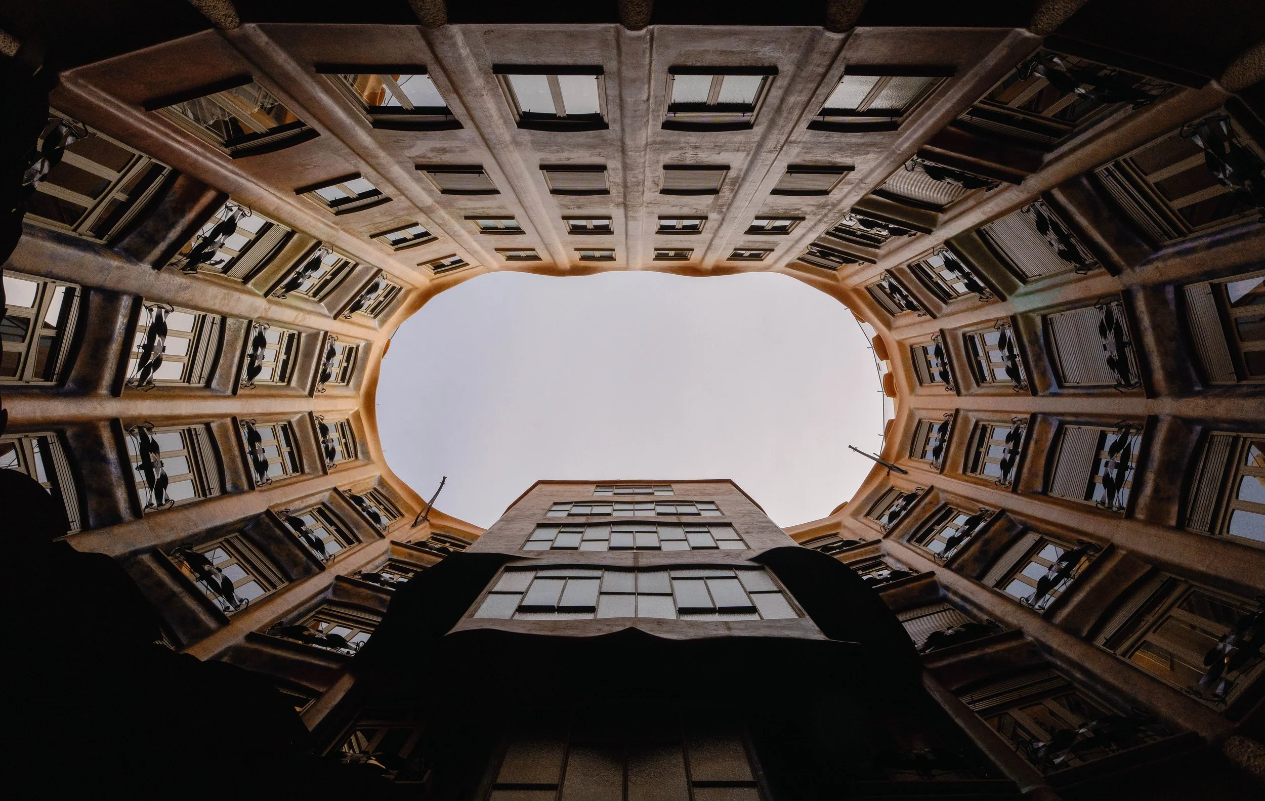 Looking up at the courtyard of a building with multiple floors, windows, balconies, and railings, with the sky visible at the top.