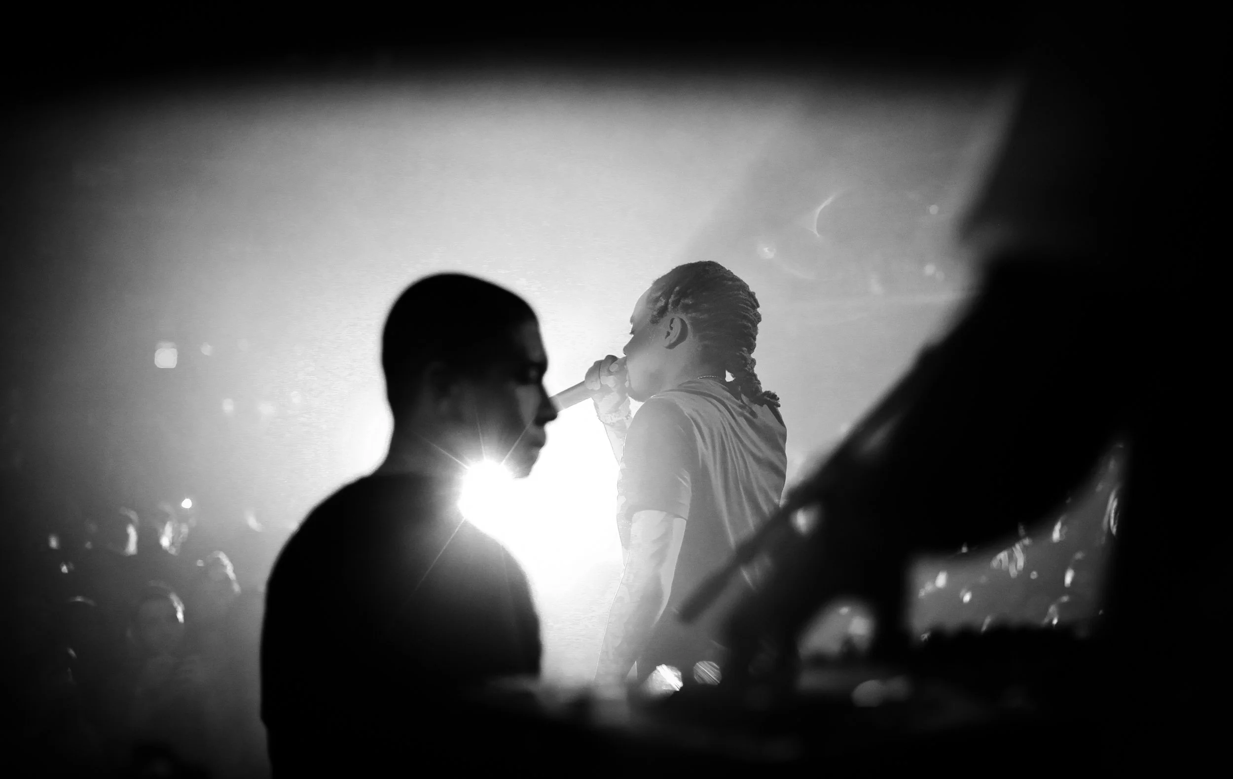 Black-and-white photograph of a singer performing on stage, with silhouettes of audience members in the foreground.