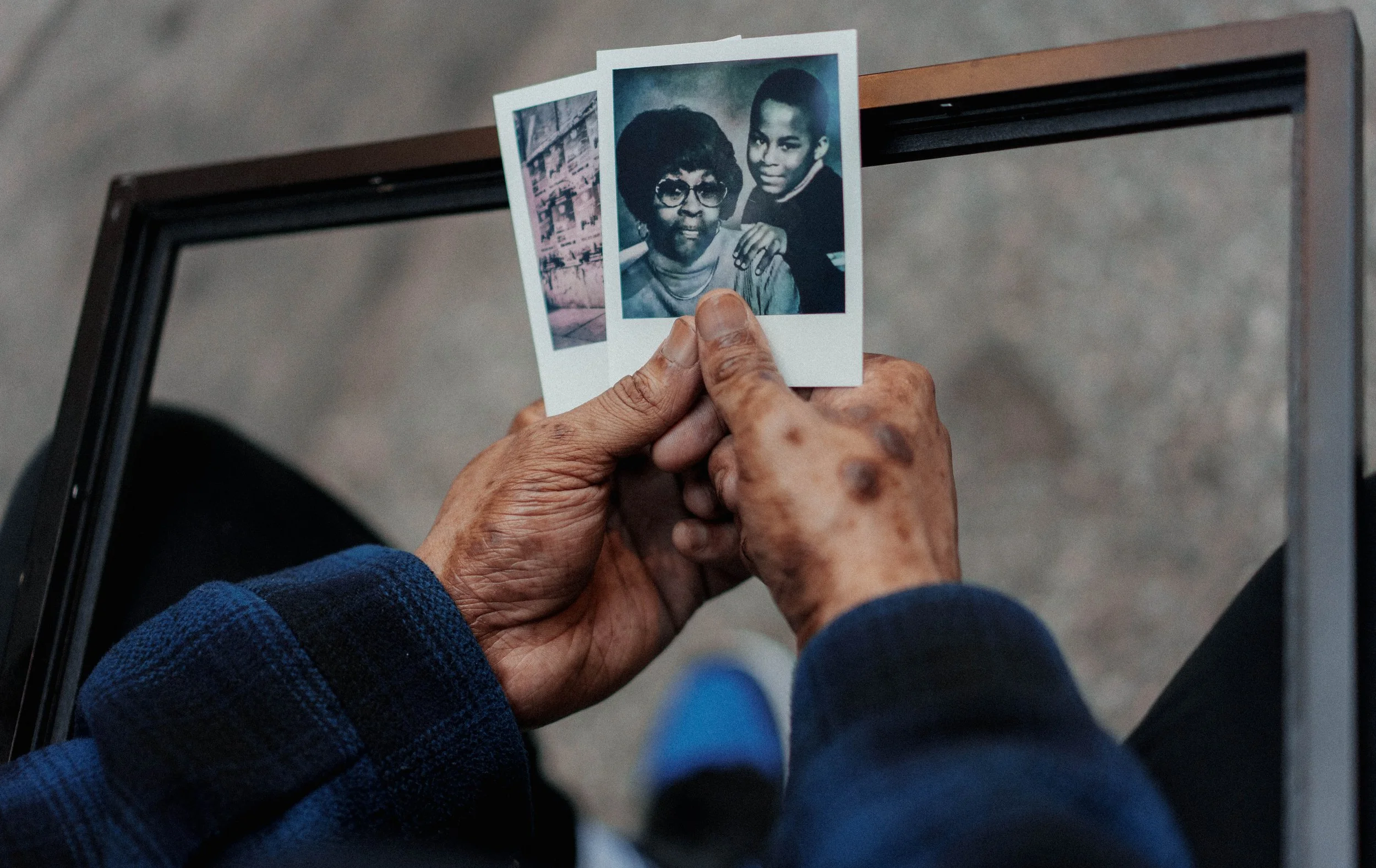 A person holding two vintage photographs, one showing a woman with glasses and a young girl, set against a gray background.