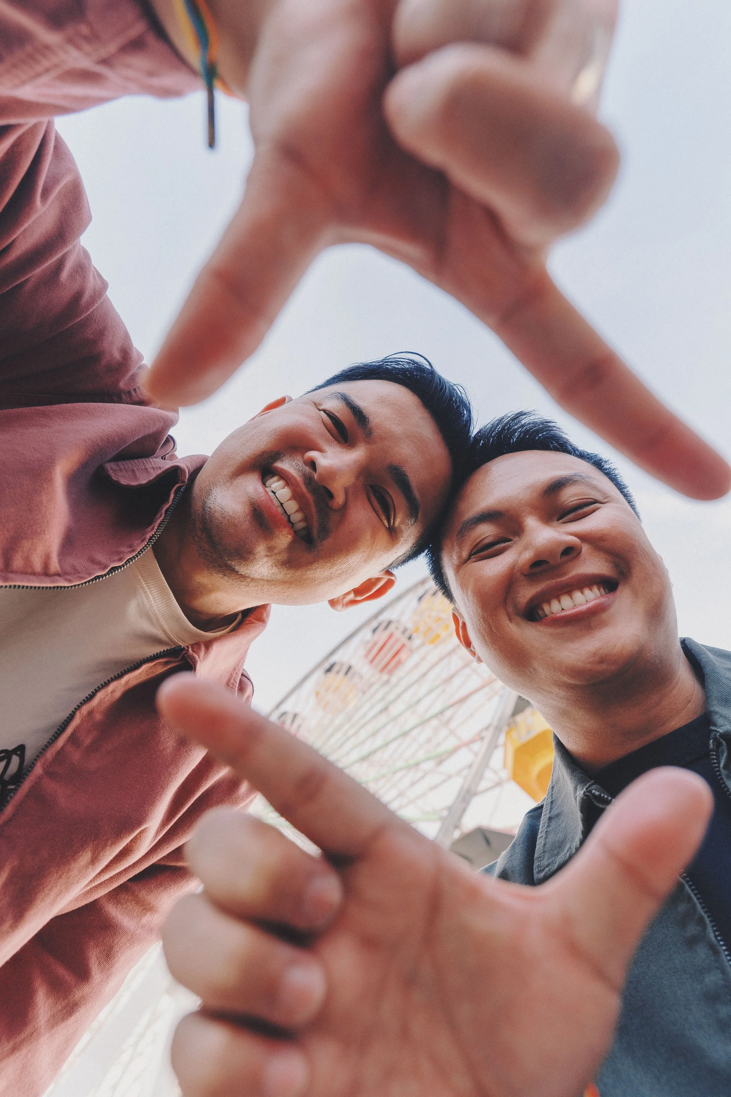 Two young men smiling and taking a photo together from below, with one person's hand reaching towards the camera in the foreground.