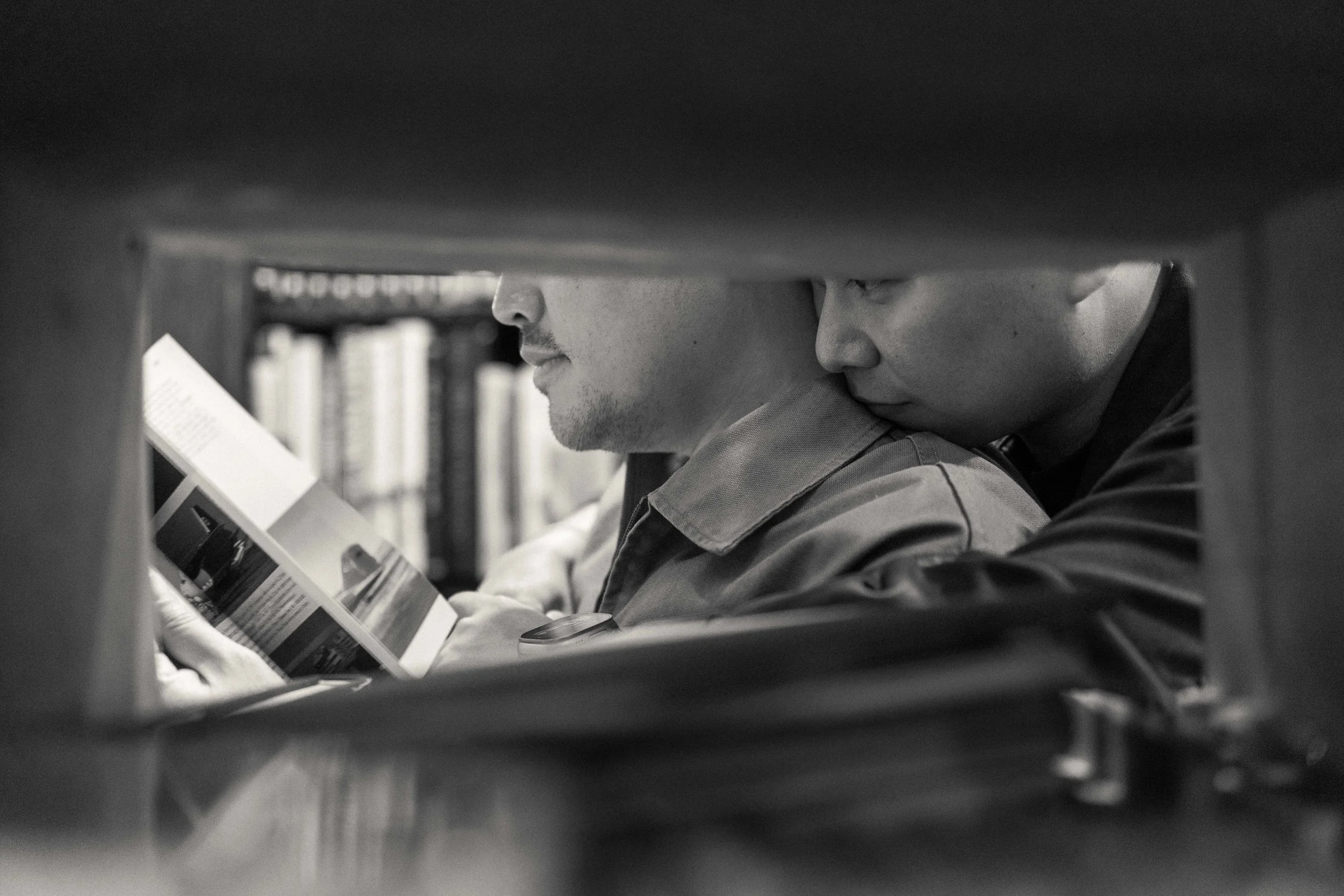 Two men are closely inspecting a product on a shelf in a store, seen through a gap