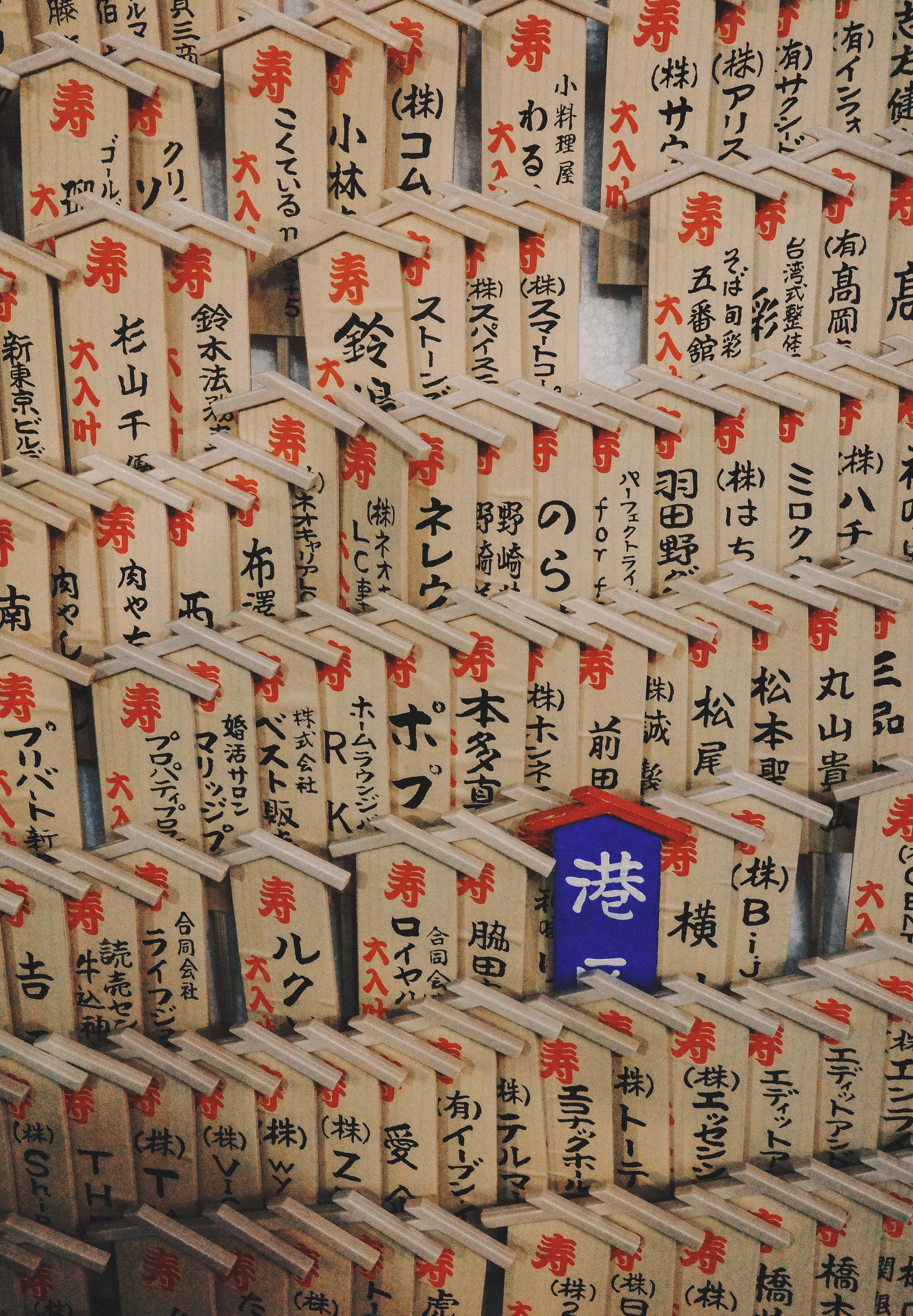 Numerous small wooden plaques with Japanese writing and red symbols, hanging on a display.