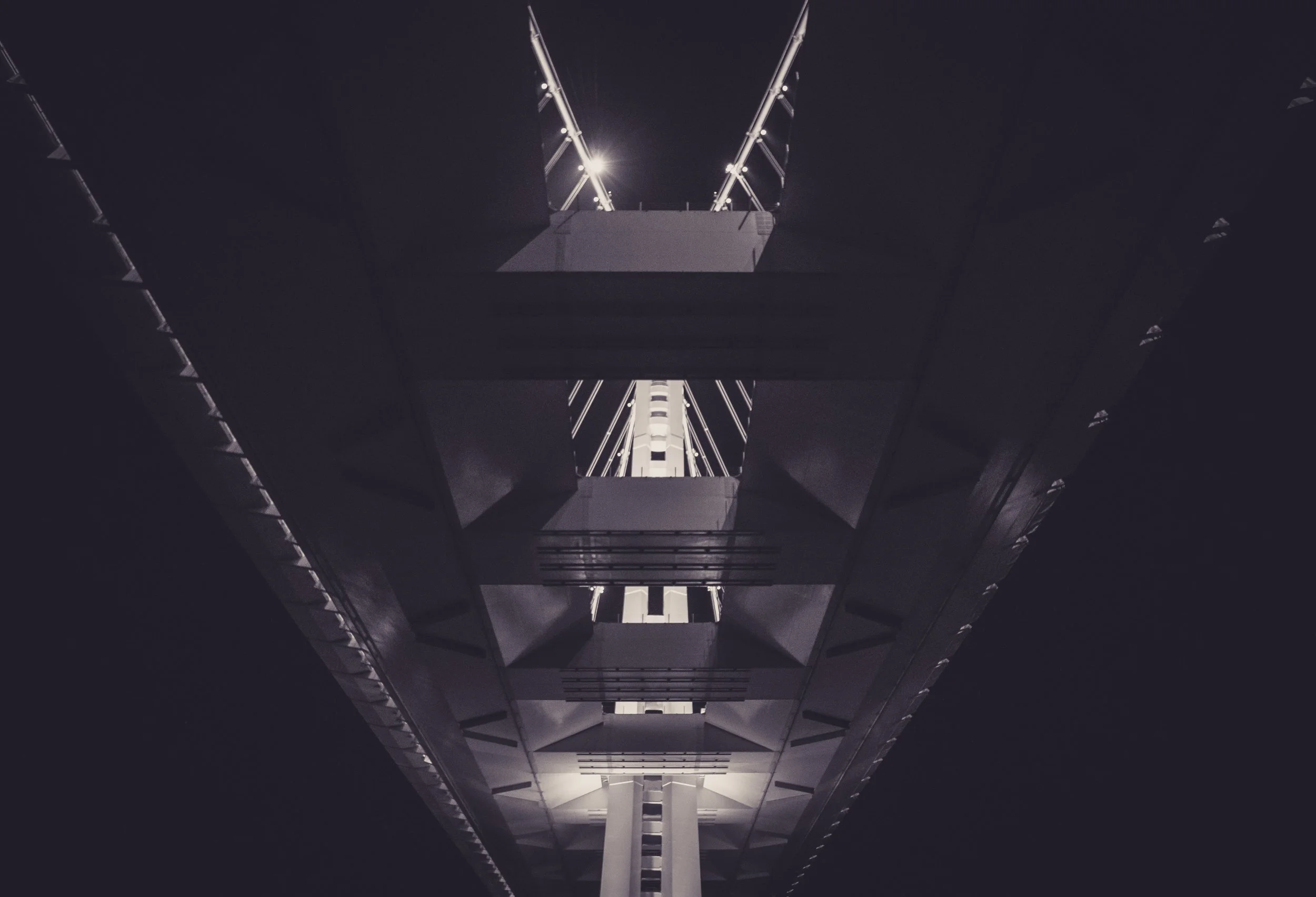 Looking up at the structure of a modern skyscraper with bright lights illuminating the sharp angles of its white facade against a dark night sky.