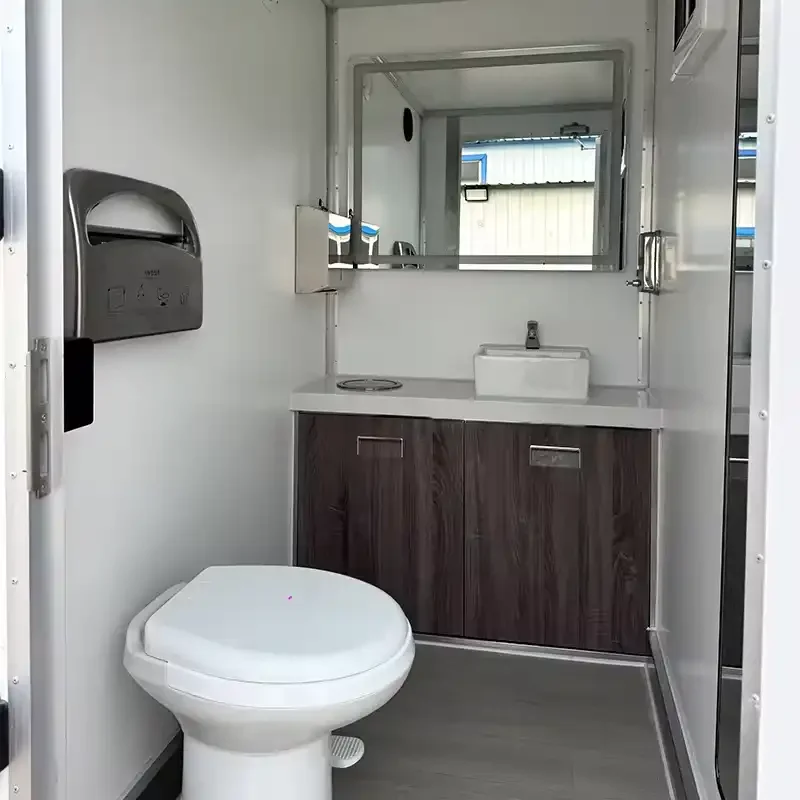 Small mobile restroom with a toilet, a vanity with a sink, a mirror, and a paper towel dispenser.