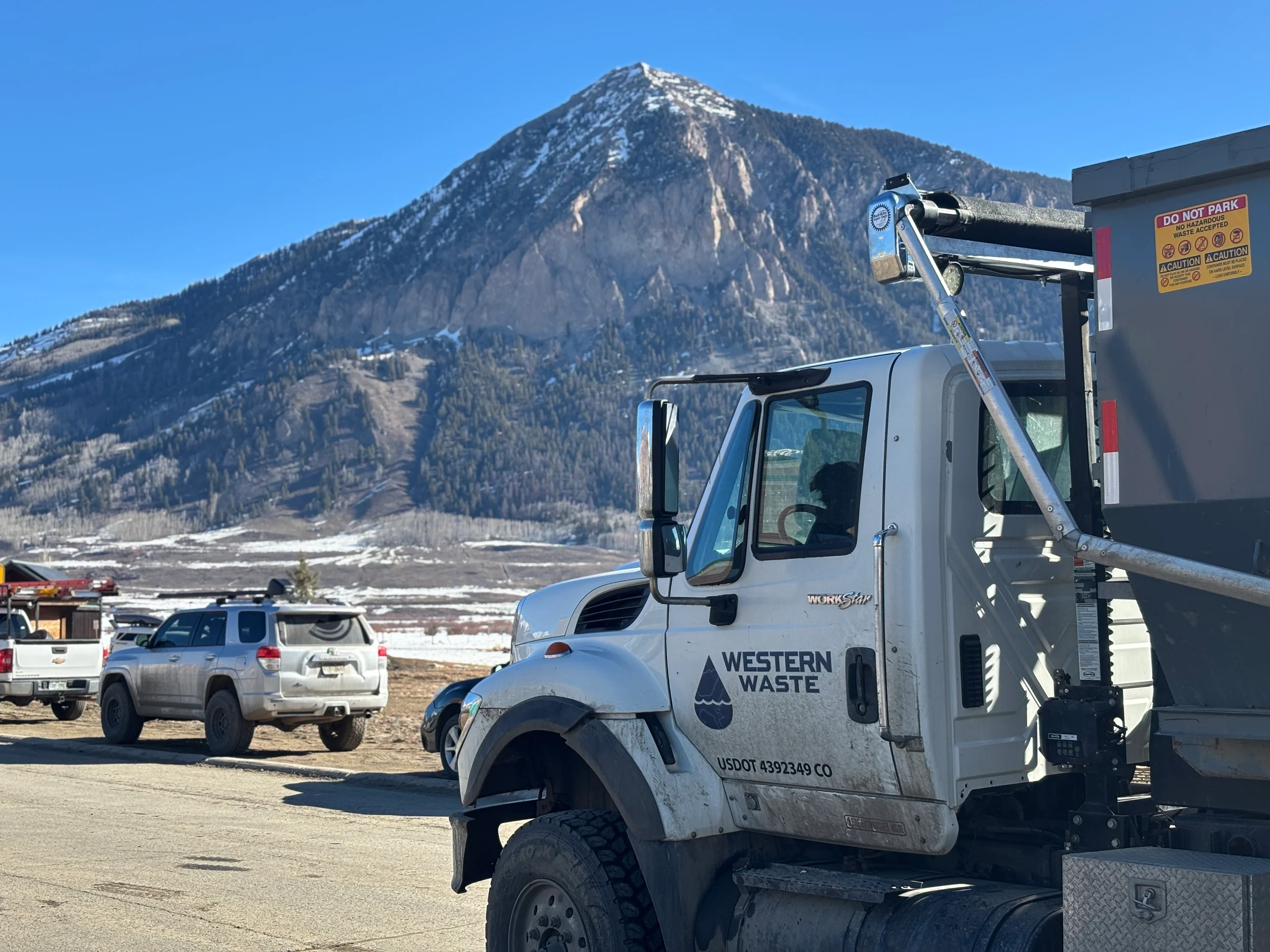 A waste collection truck labeled 'Western Waste' with a mountain and blue sky in the background.
