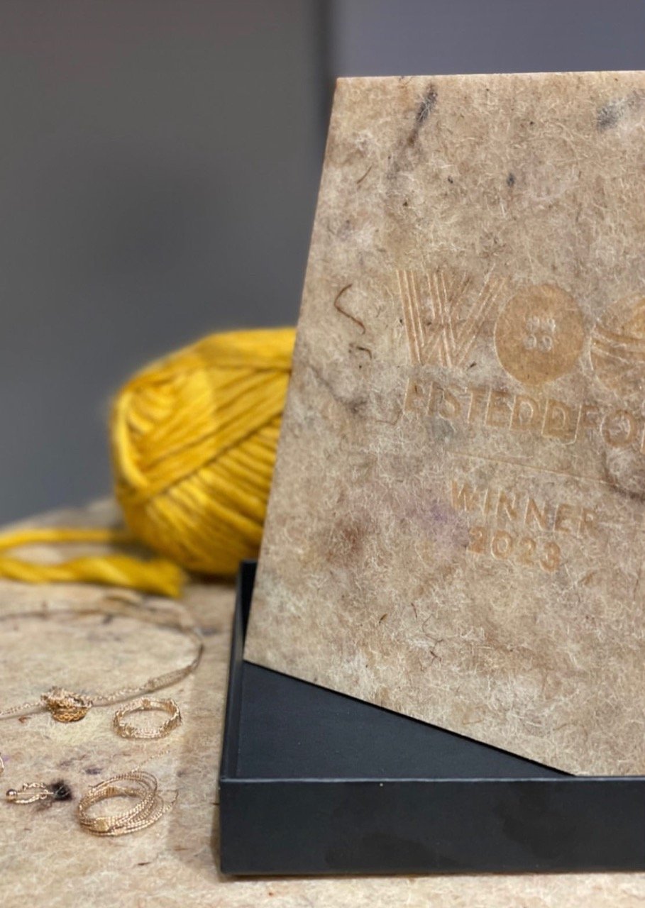 Close-up of a beige card with royal engraving, standing on a black stand, with yellow yarn and gold jewelry on the surface nearby.