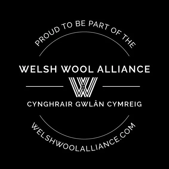 A black background with white text that reads "Proud to be part of the Welsh Wool Alliance" and "cynghrai gwlân Cymru." The center features a stylized "W" logo and the website welshwoolalliance.com.
