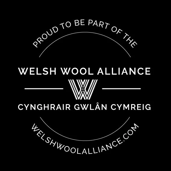 Black background with white text and logo promoting the Welsh Wool Alliance. Text includes 'Proud to be part of the Welsh Wool Alliance' and the website welshwoolalliance.com, with the Welsh translation of the phrase.