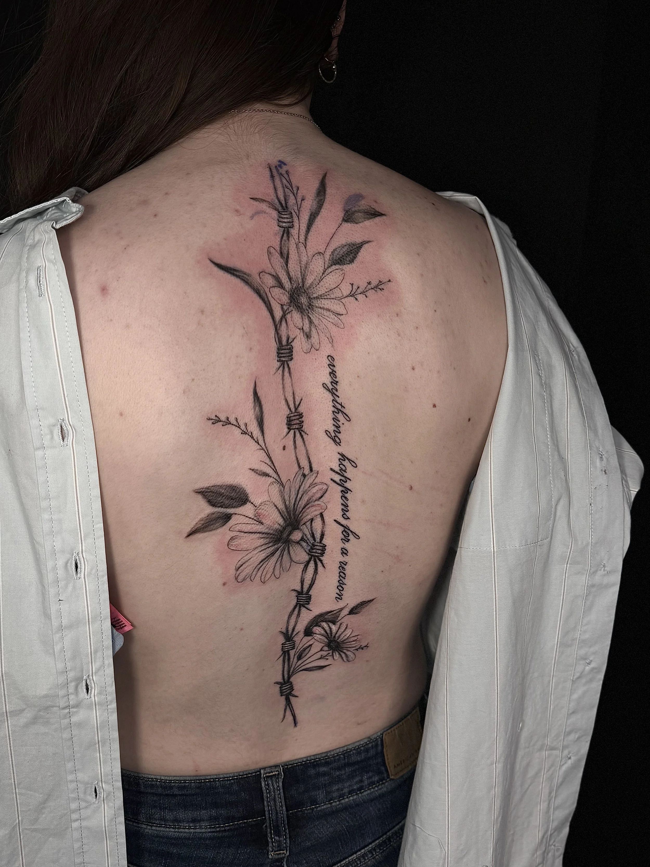 Tattoo of flowers and barbed wire on a person's shoulder and upper back.