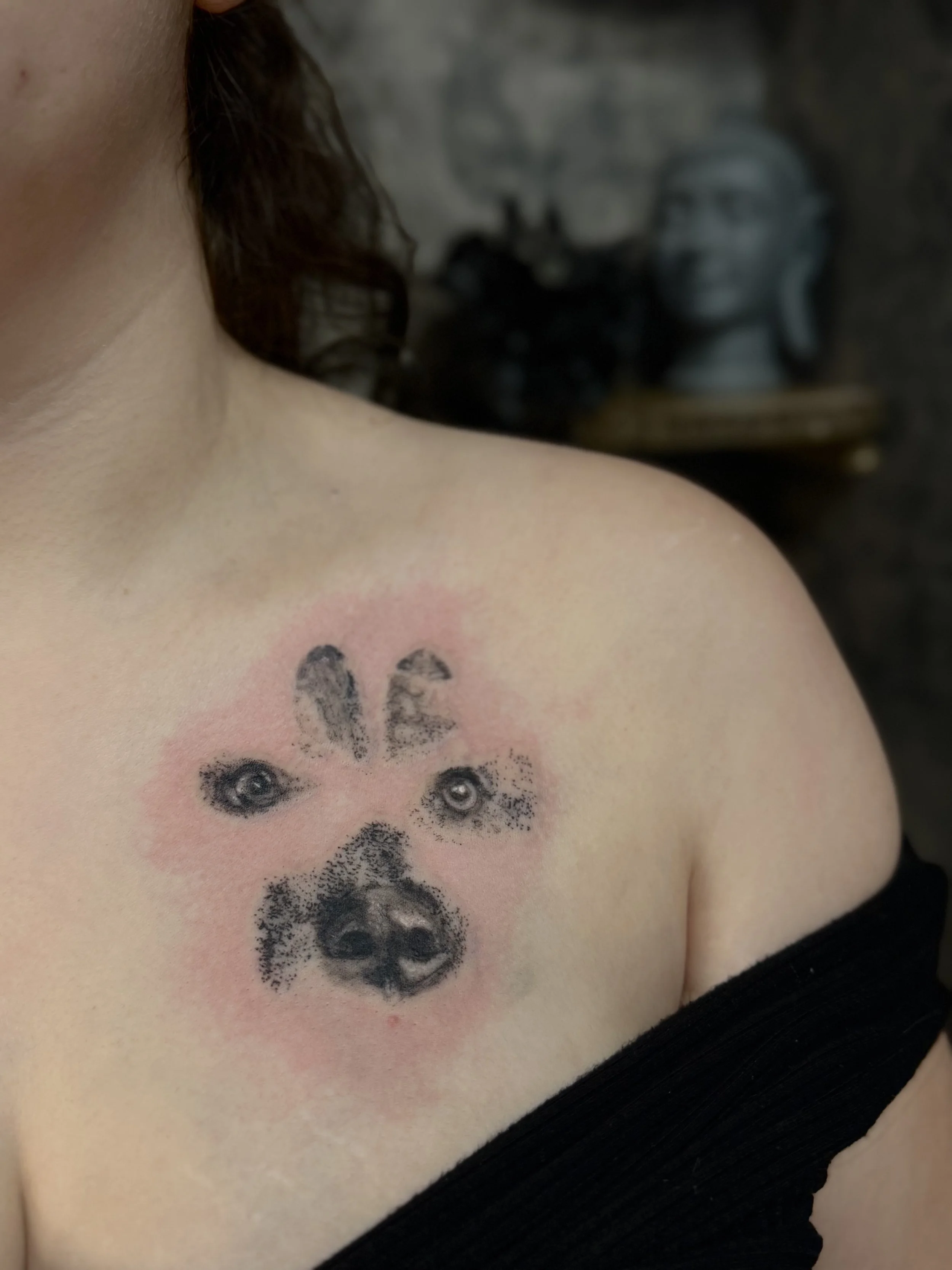 Close-up of a person's shoulder and upper arm with a tattoo of multiple pairs of detailed eyes and paw prints surrounded by pink shading.