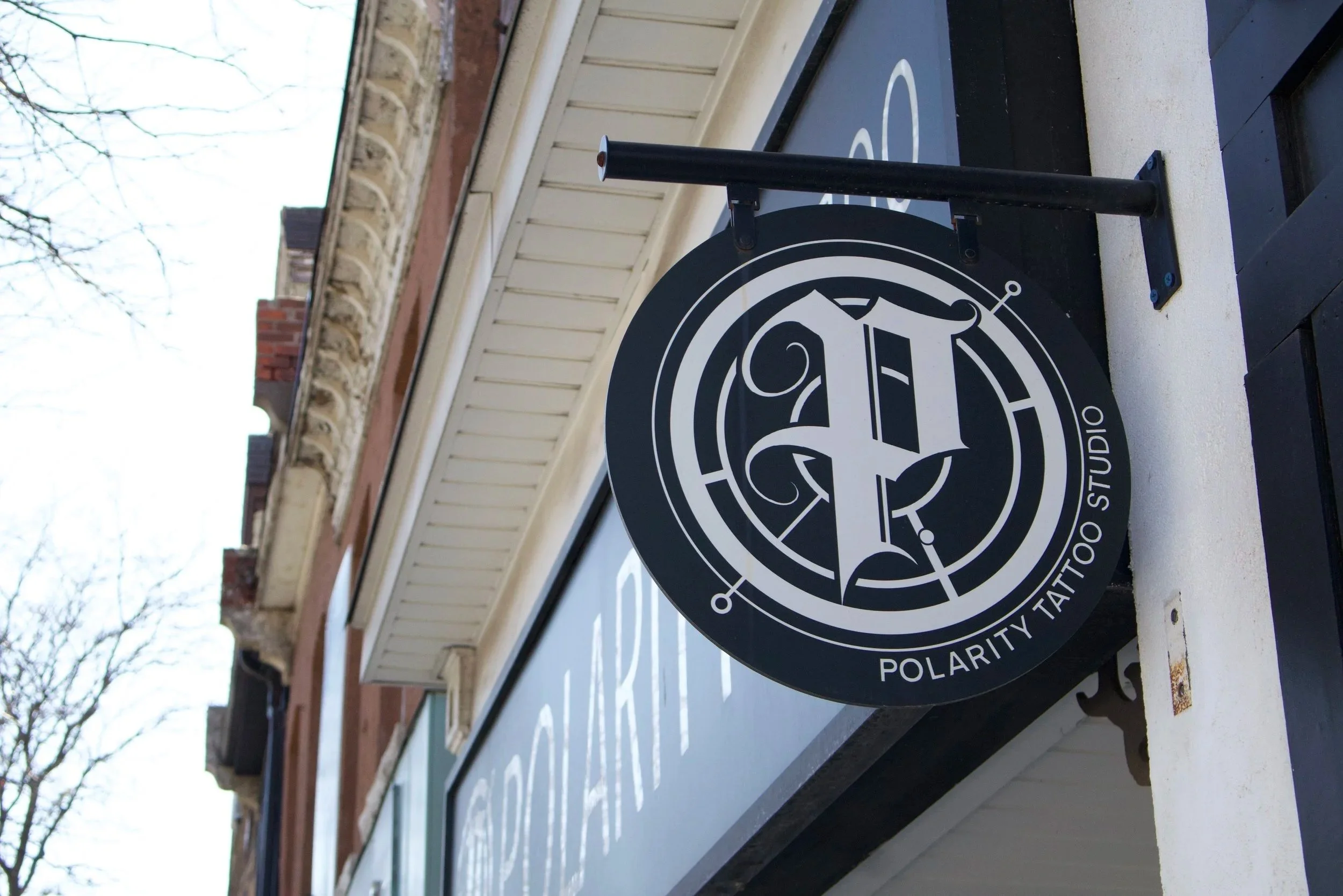 Black circular sign with white design, mounted on a black pole, attached to a building's exterior wall, with some brown and red brick in the background.