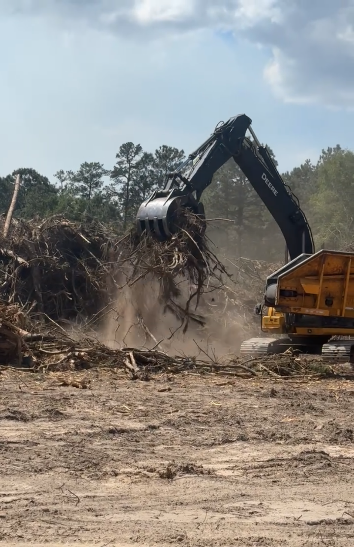 A large excavator is clearing debris and fallen trees on a construction or land clearing site.