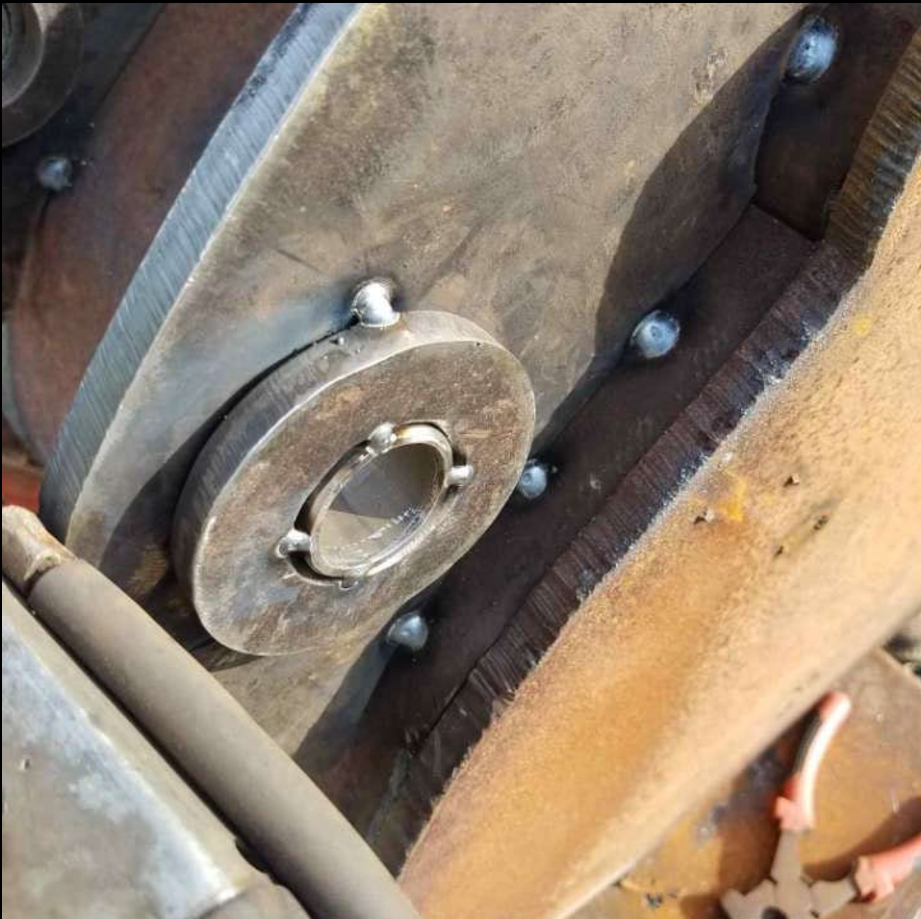 Close-up of a metal component, possibly a part of a machine or engine, with visible bolts and a circular opening, mounted on a rusted metal surface.