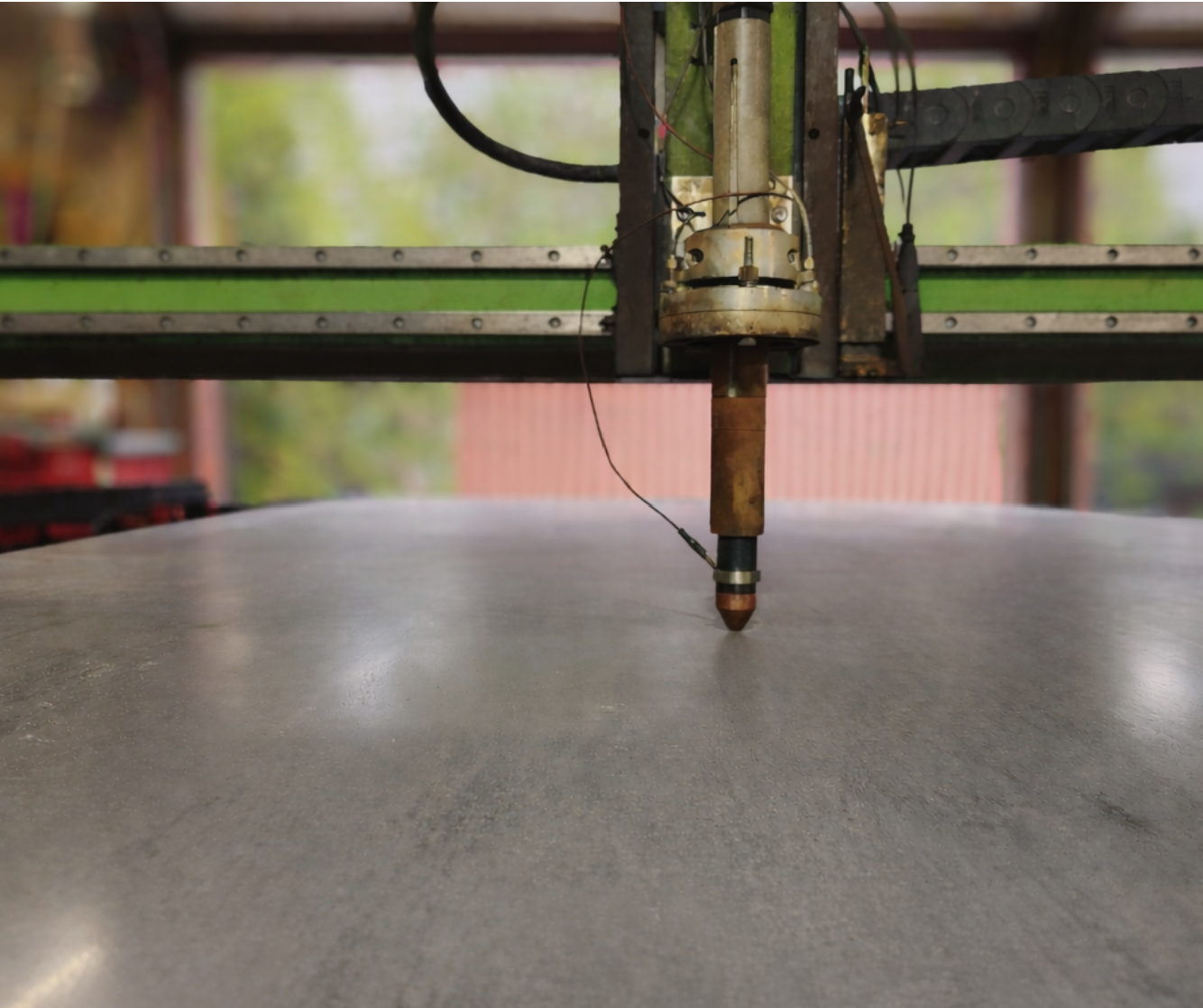 Close-up of a CNC machine cutting a round piece of material, with the cutting bit positioned downward and industrial equipment visible in the background.