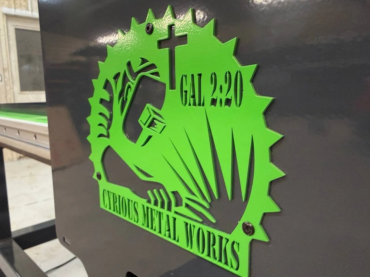 Green metal sign displaying 'GALL 2.20', 'CURIOUS METAL WORMS', and a graphic of a clownfish with an antenna, mounted on a dark surface.