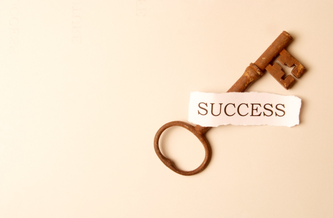 An old rusty key with a torn paper label reading "SUCCESS" attached to it on a light beige background.