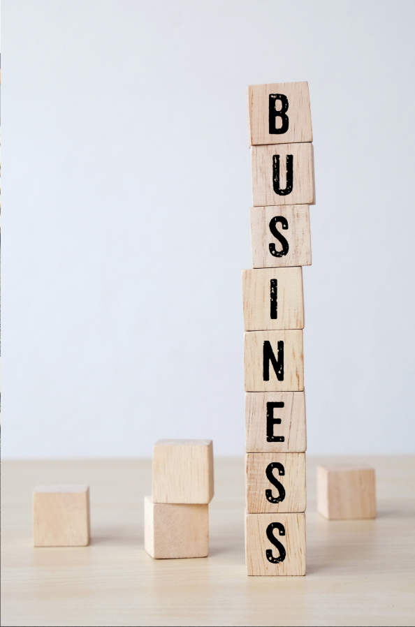 Wooden blocks spelling 'BUSINESS' stacked vertically, with a few blocks scattered on a light wooden surface.