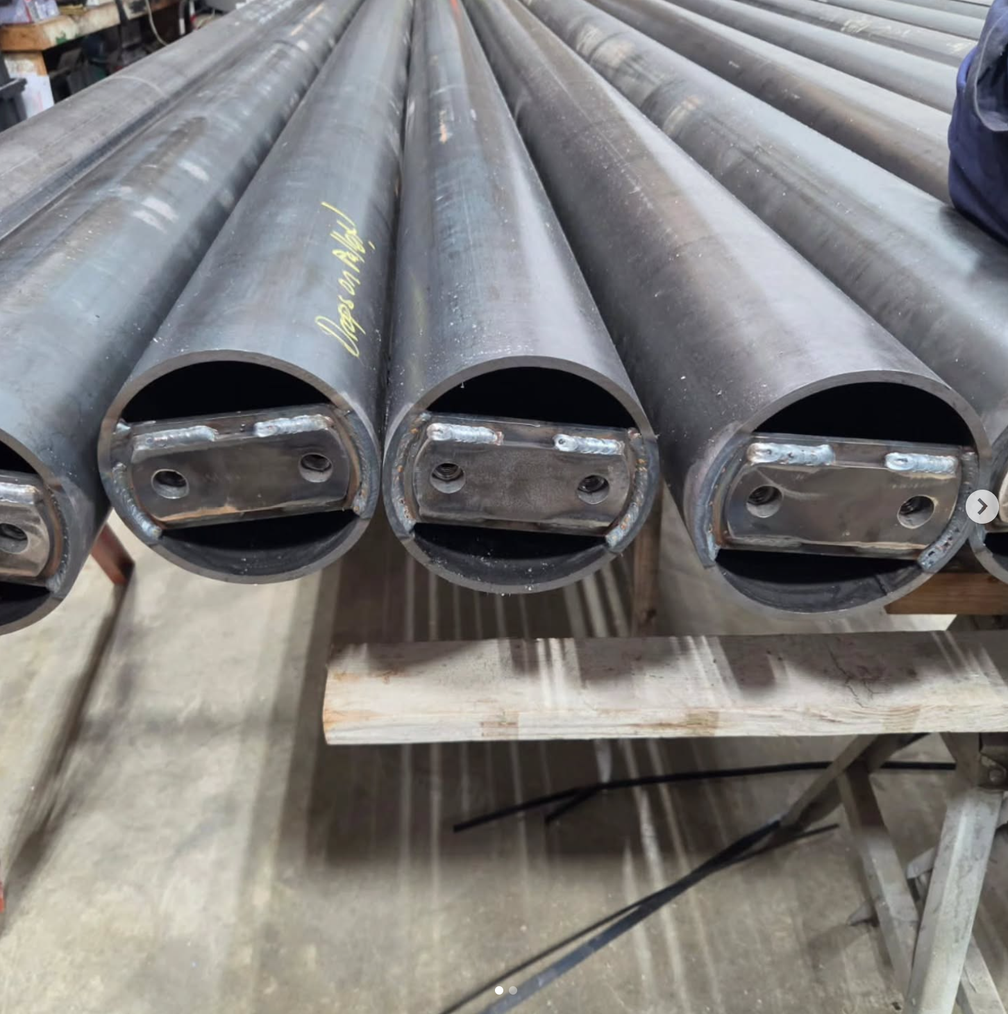 Close-up of large metal pipes with welded ends, placed on a wooden workbench in a workshop.
