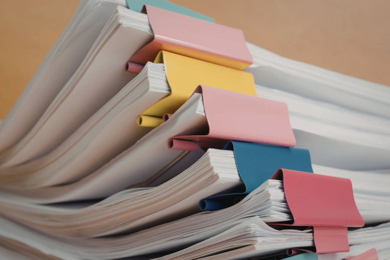 A stack of paper documents with colorful paper clips and dividers in pink, yellow, and blue.