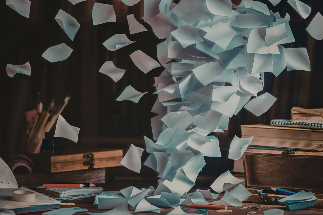 Paper notes falling onto a cluttered desk with notebooks, pens, and office supplies.