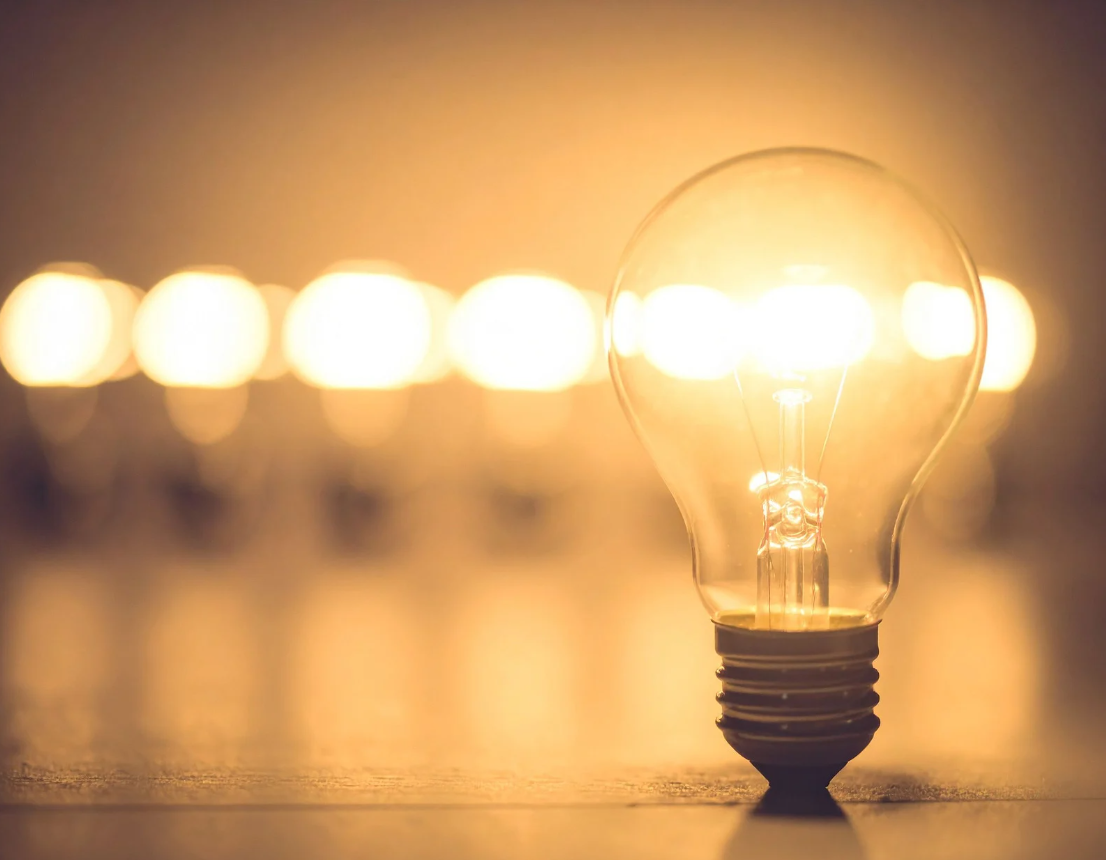 A glowing incandescent light bulb with several blurred light bulbs in the background.