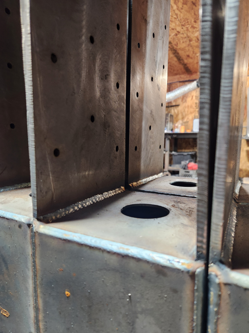 Close-up of metal welded structures with drilled holes, likely part of a metal fabrication or welding project in a workshop.
