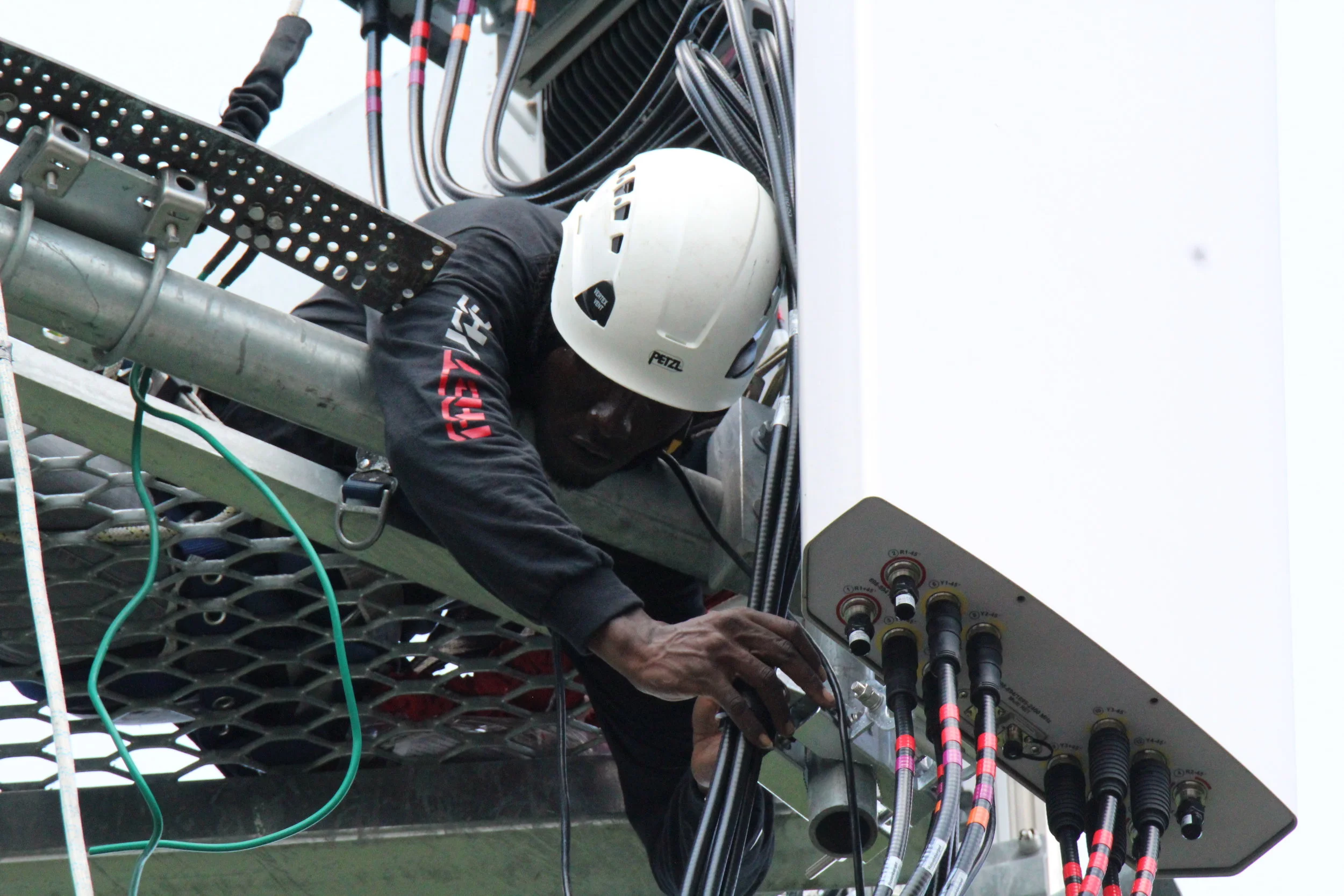 A technician wearing a white helmet working on electrical connections on a large industrial machine.