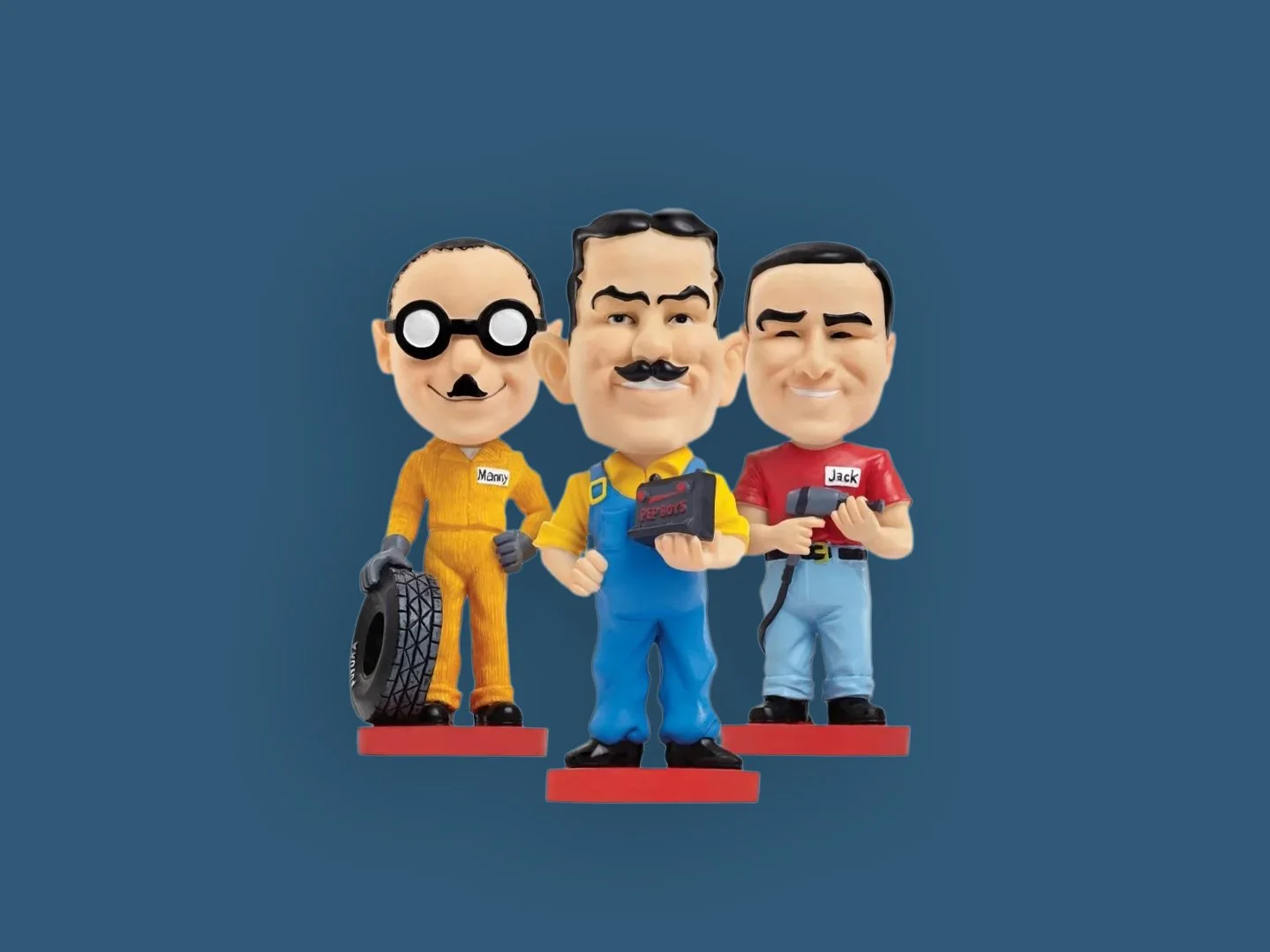 Three cartoon-style figurines resembling characters from the animated series "The Big Bang Theory" with exaggerated facial features, standing on red bases against a blue background. The left figure has glasses and a mustache, dressed in a yellow jumpsuit, holding a tire. The middle figure has a mustache, holding a camera, and is dressed in blue overalls. The right figure has short hair, holding a remote, and wears a red shirt and blue jeans. All three have labels on their shirts: "Mary," "Penny," and "Jack."