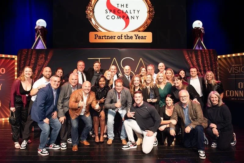 Group of people at an awards event, with a large screen displaying 'The Specialty Company' and 'Partner of the Year'