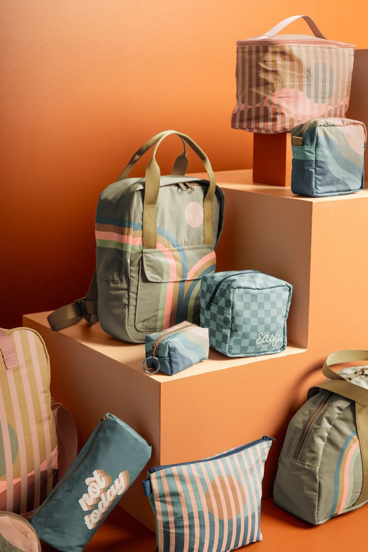 Display of pastel-colored bags and pouches with abstract patterns on peach-colored display stands.