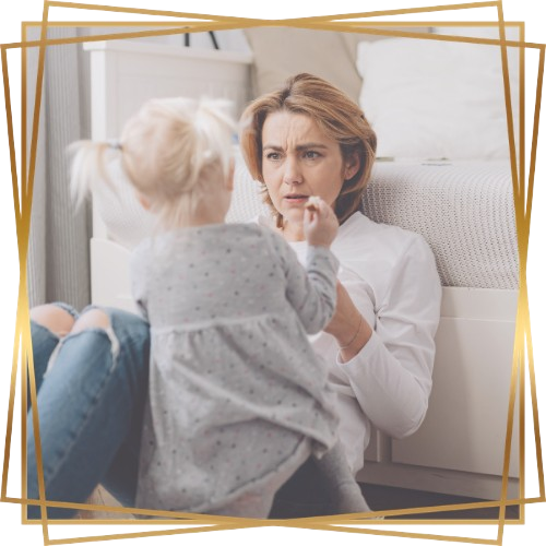 Woman parent with short red hair in jeans sitting on floor with her blonde daughter in pigtails in gray dress