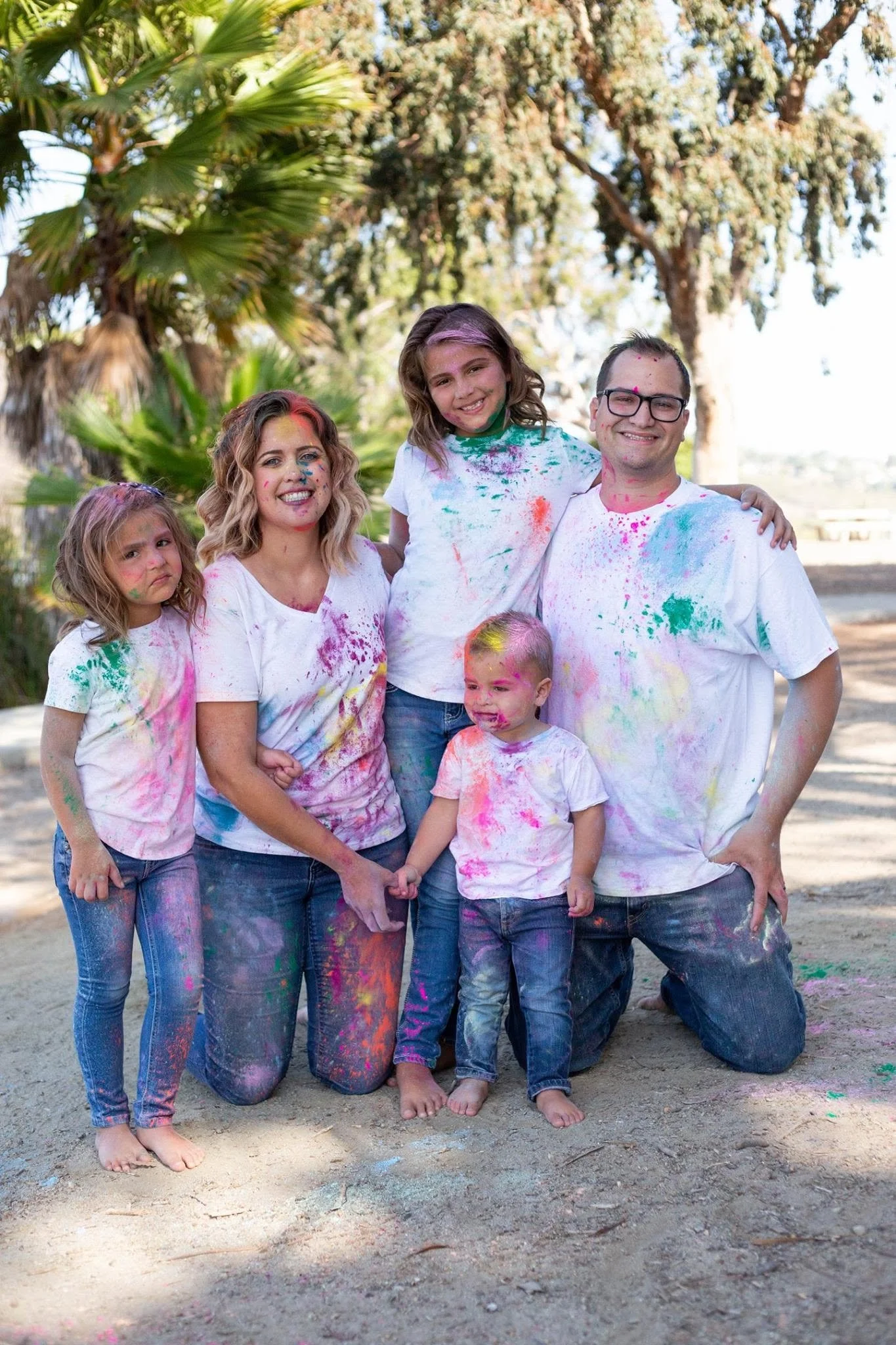 Matti Mattilyn Millman Kneeling with her Family all in White T-Shirt and Jeans Covered in Vibrant Colored Powder