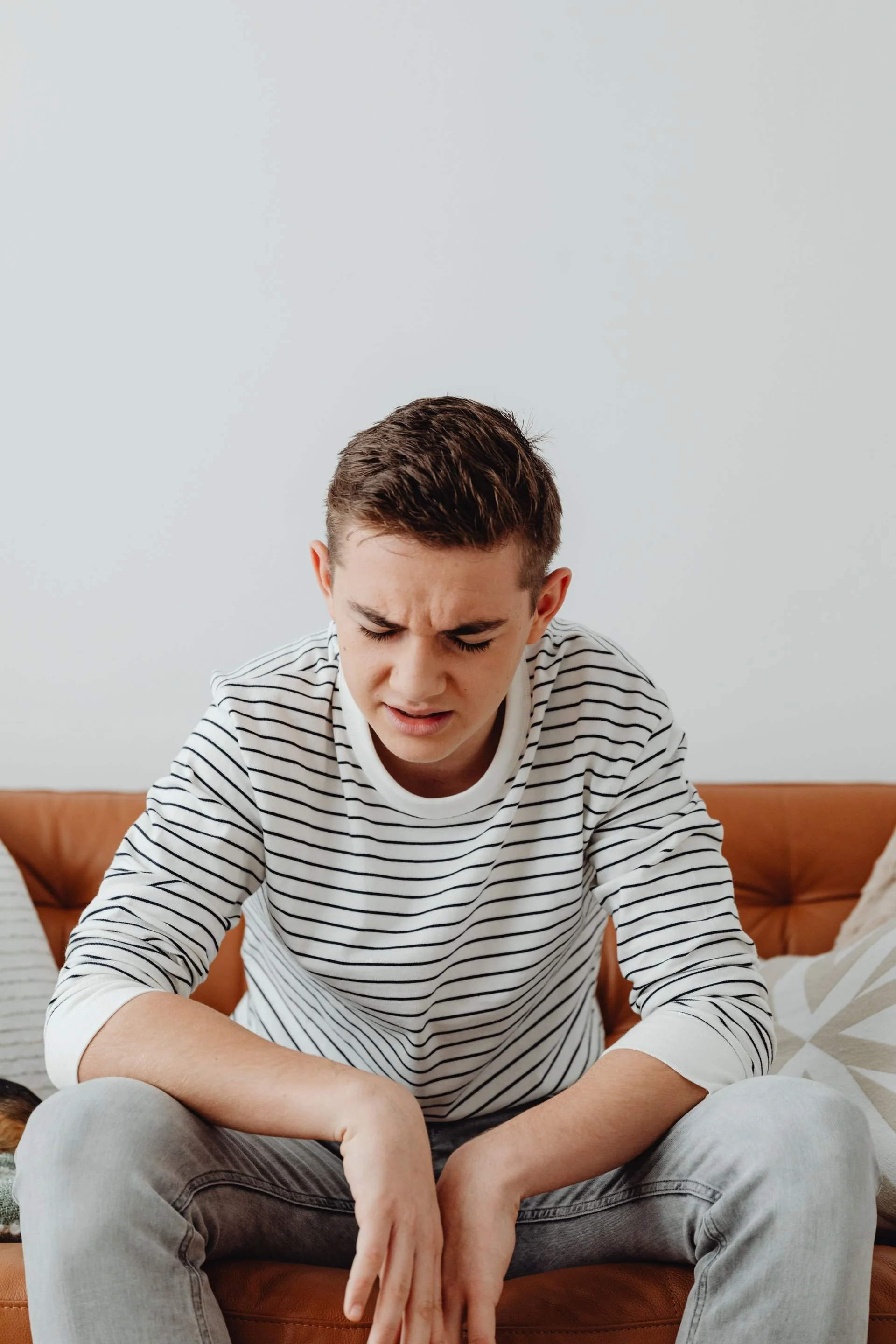 Young adult teenager with brown hair wearing black and white striped shirt and gray jeans hanging his shoulders