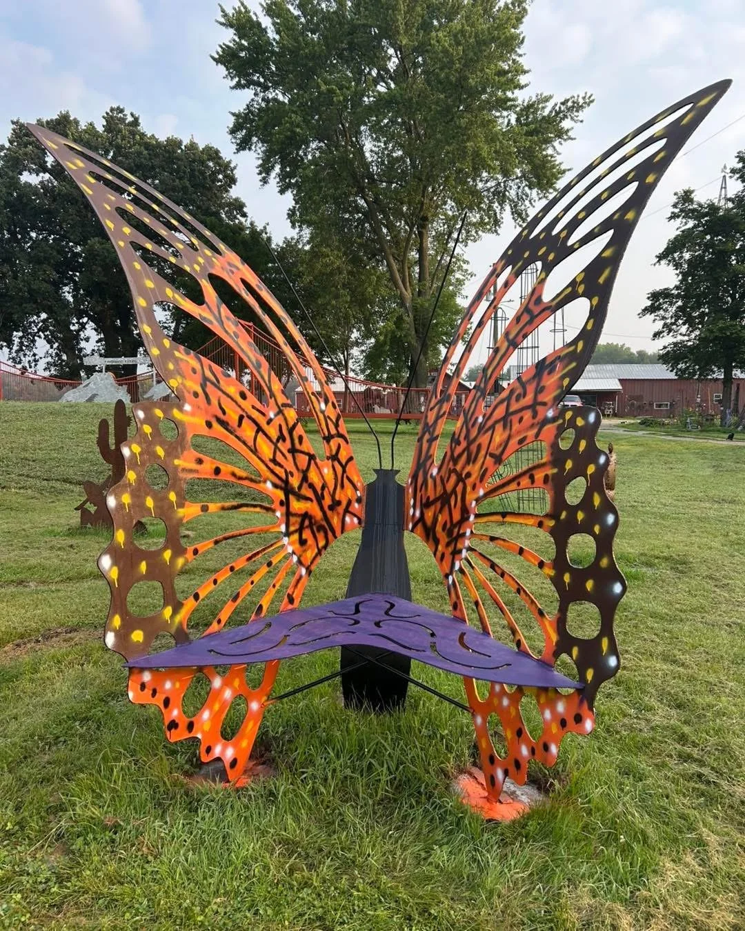 Colorful butterfly-shaped sculpture with black, orange, and purple colors, situated on a grassy field.