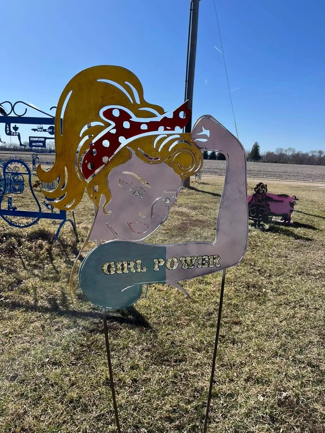 Colorful metal garden stake of a girl with blonde hair styled in a curl, wearing a red polka-dot bandana, and a sleeveless top with the words 'GIRL POWER'.