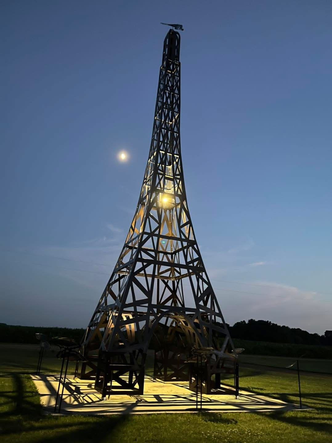 A metal tower structure under a twilight sky with the moon visible, illuminated by lights