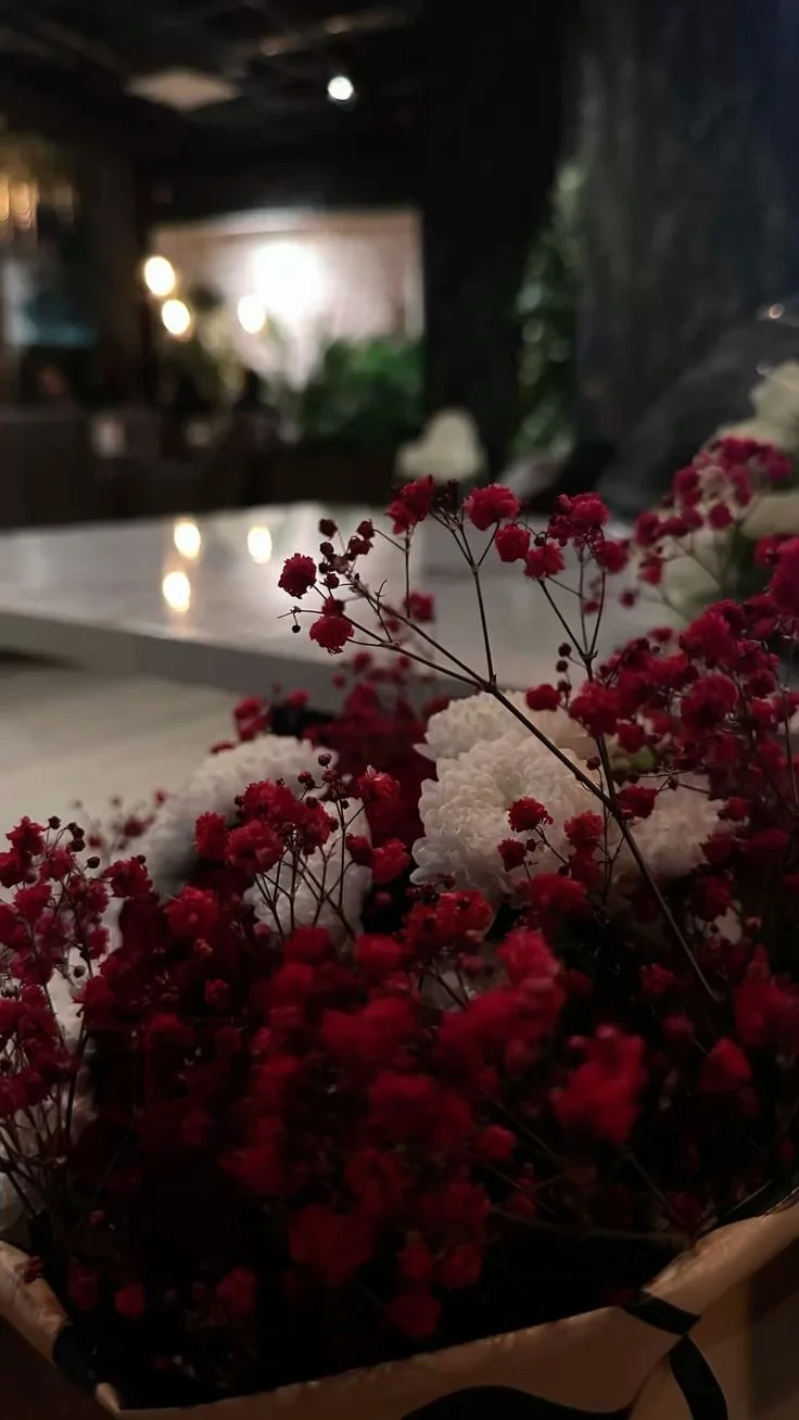 Close-up of red and white flowers, likely baby's breath, on a table in a dimly lit room with blurred background.