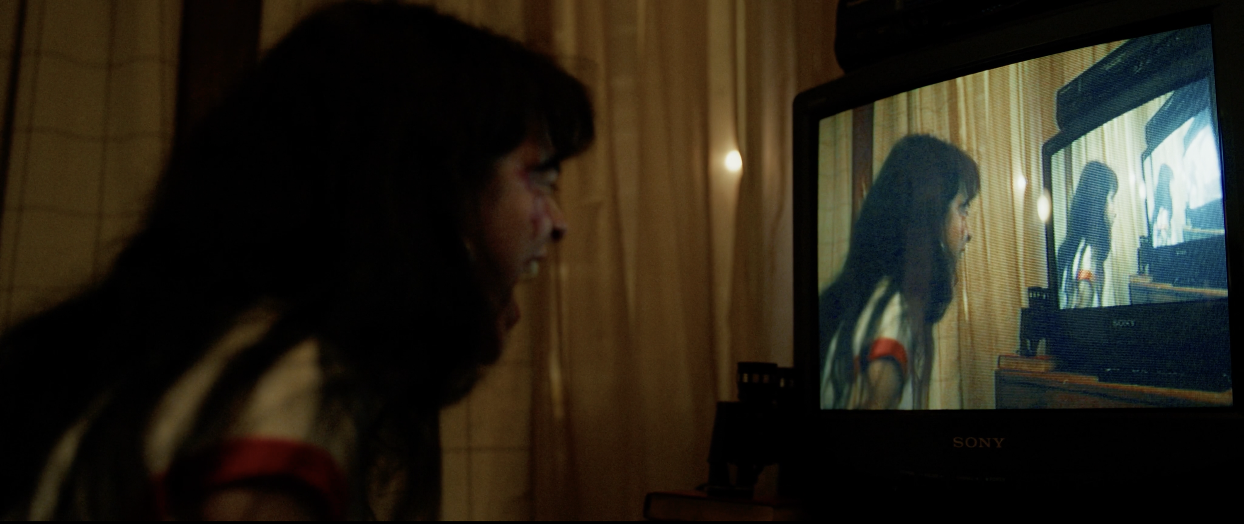 A person with long dark hair watching a television in a dimly lit room.