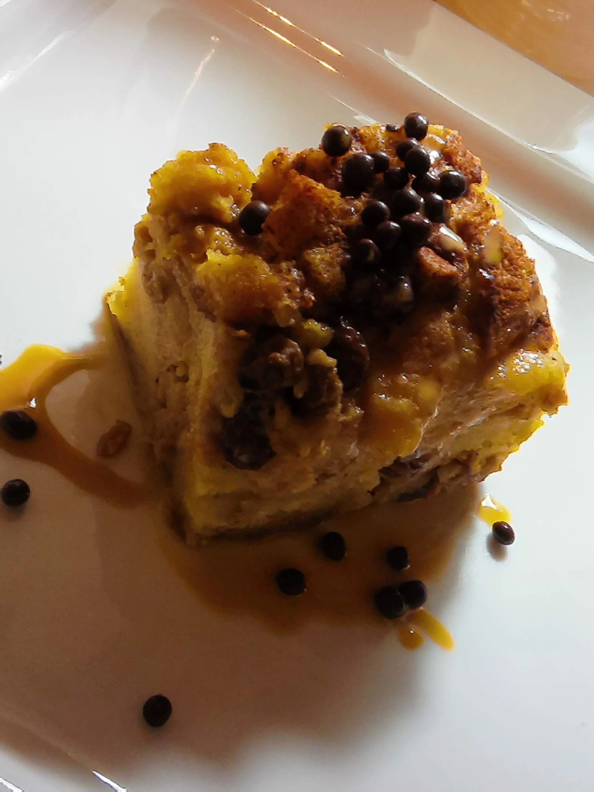 Sweet Potato-infused bread pudding with chocolate-covered quinoa balls, drizzled with dolce di leche, served on a white plate.