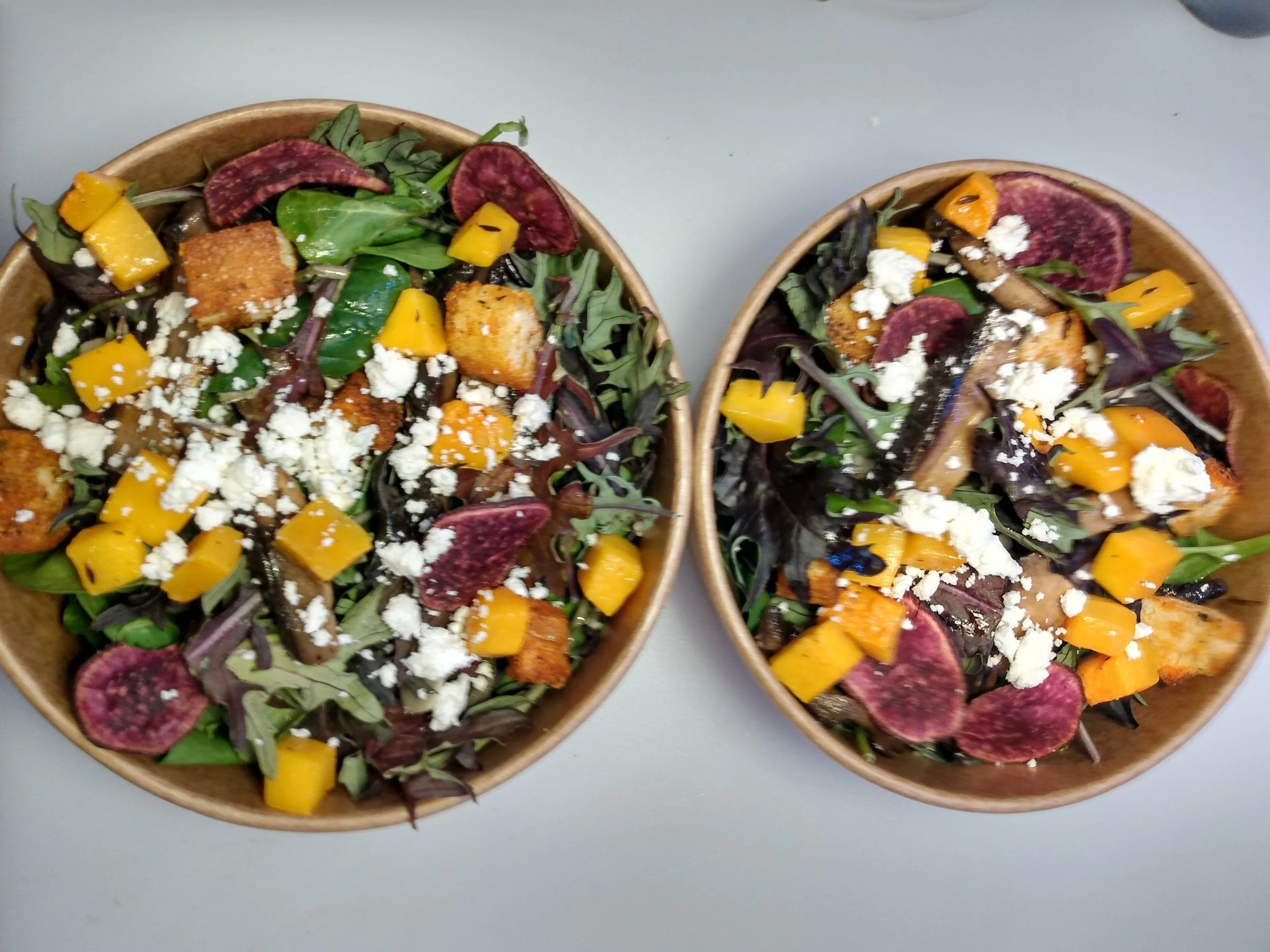 Two bowls of mixed salad with greens, roasted sweet potatoes, crispy tofu, and crumbled cheese.