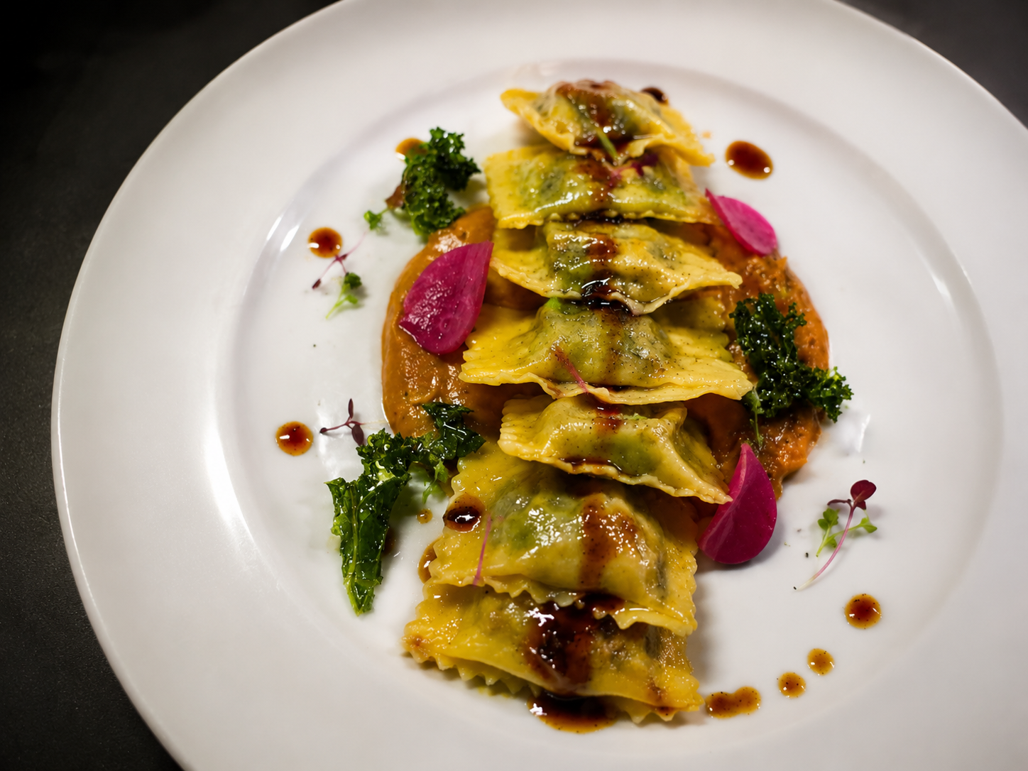 A beautiful, colorful plate of Smoked Jerk Chicken stuffed Agnolotti, served atop a Burnt Carrot & Bourbon Puree. Garnished with pickled radishes, kale chips...and a drizzle of Jerk demi
