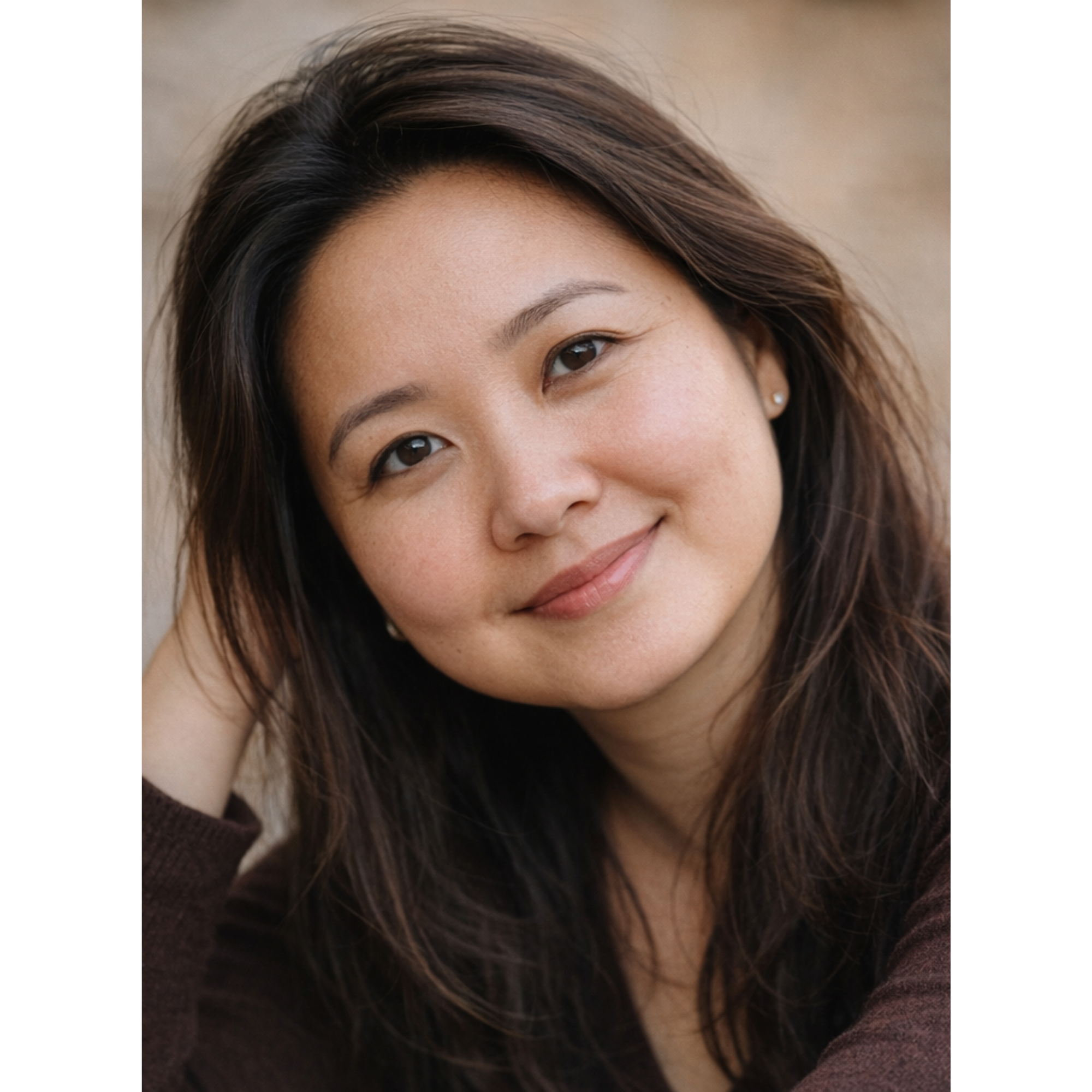 Close-up of a woman with long brown hair, brown eyes, and a small pearl earring, smiling softly.